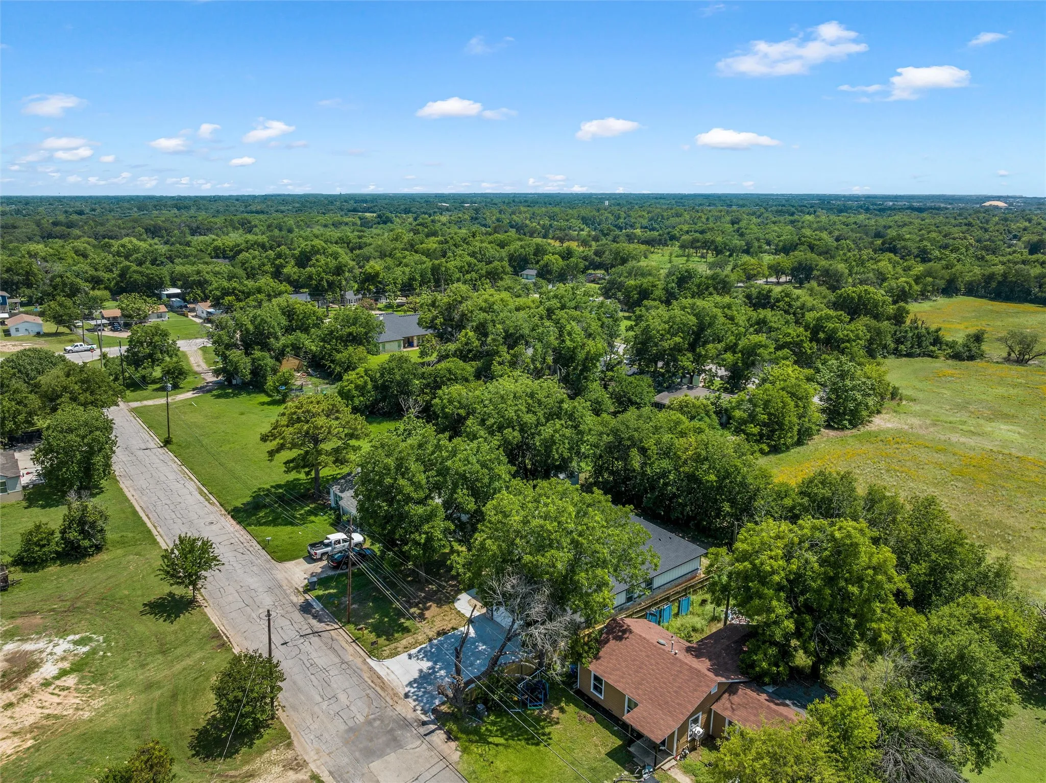 Aerial perspective showcasing a residential property with a reddish-brown roof, surrounded by mature trees