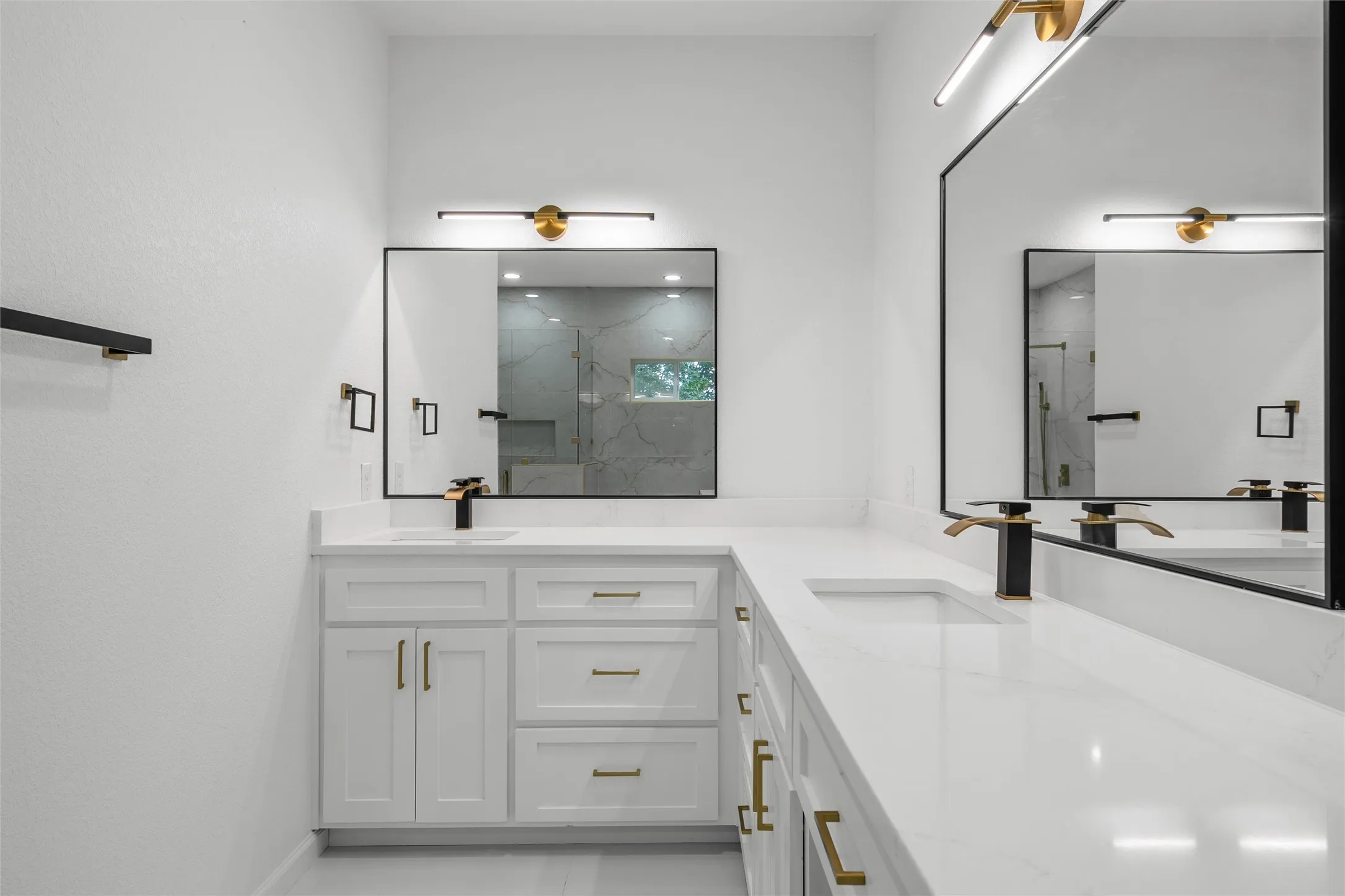 Double vanity featuring white cabinetry, integrated sinks, white countertops, black and gold fixtures, and rectangular mirrors with black frames