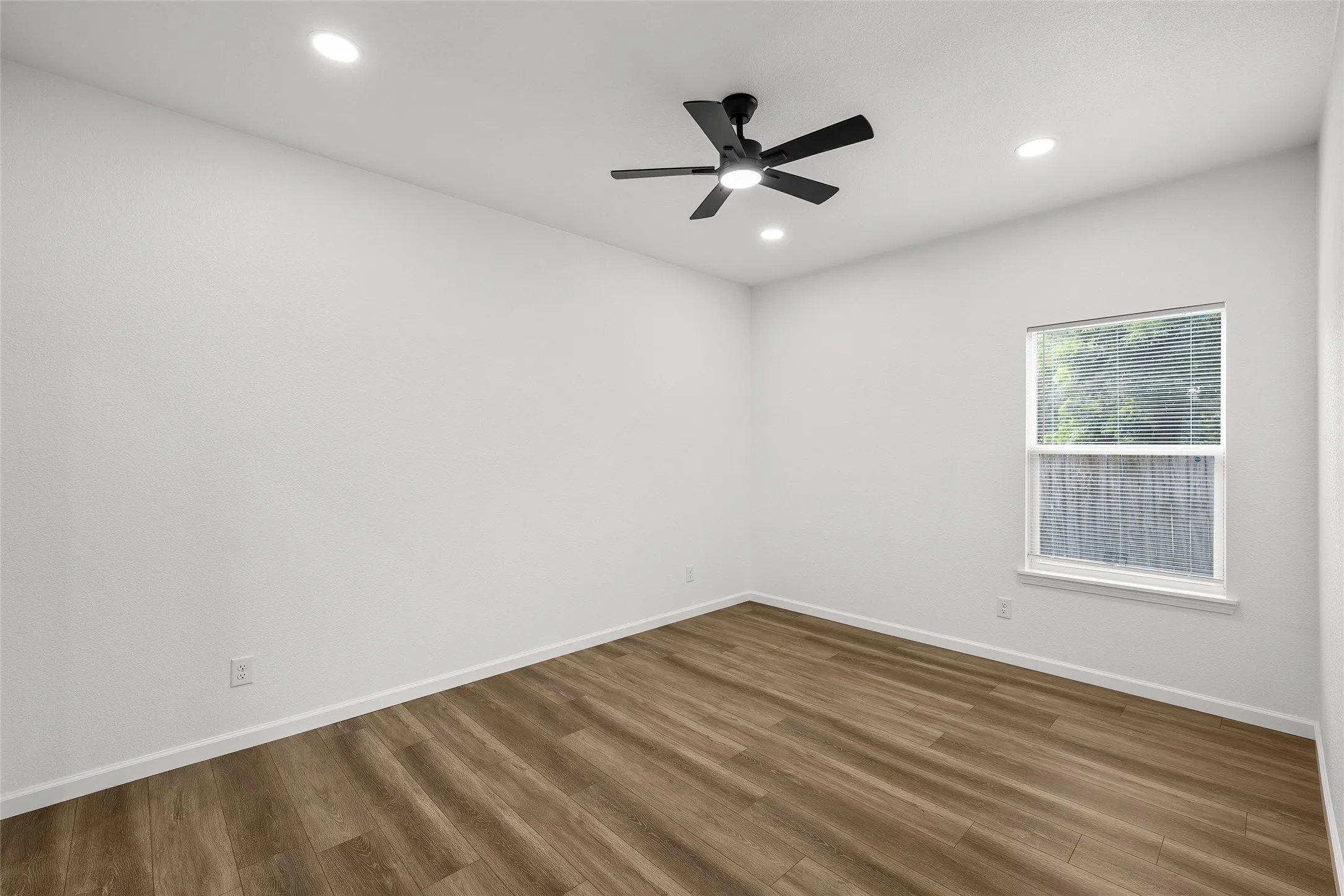 Neutral-toned room featuring wood-finish flooring, a ceiling fan with integrated lighting, and recessed ceiling lights