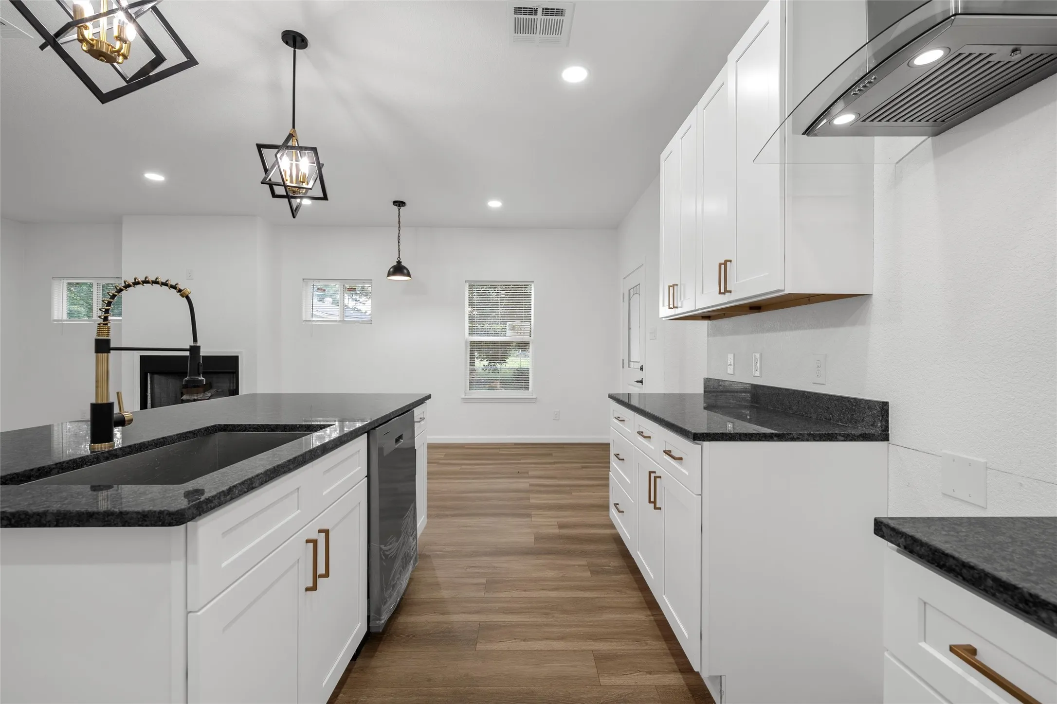 Modern kitchen featuring dark countertops, white cabinetry with bronze hardware, and a black sink with a flexible gold and black faucet