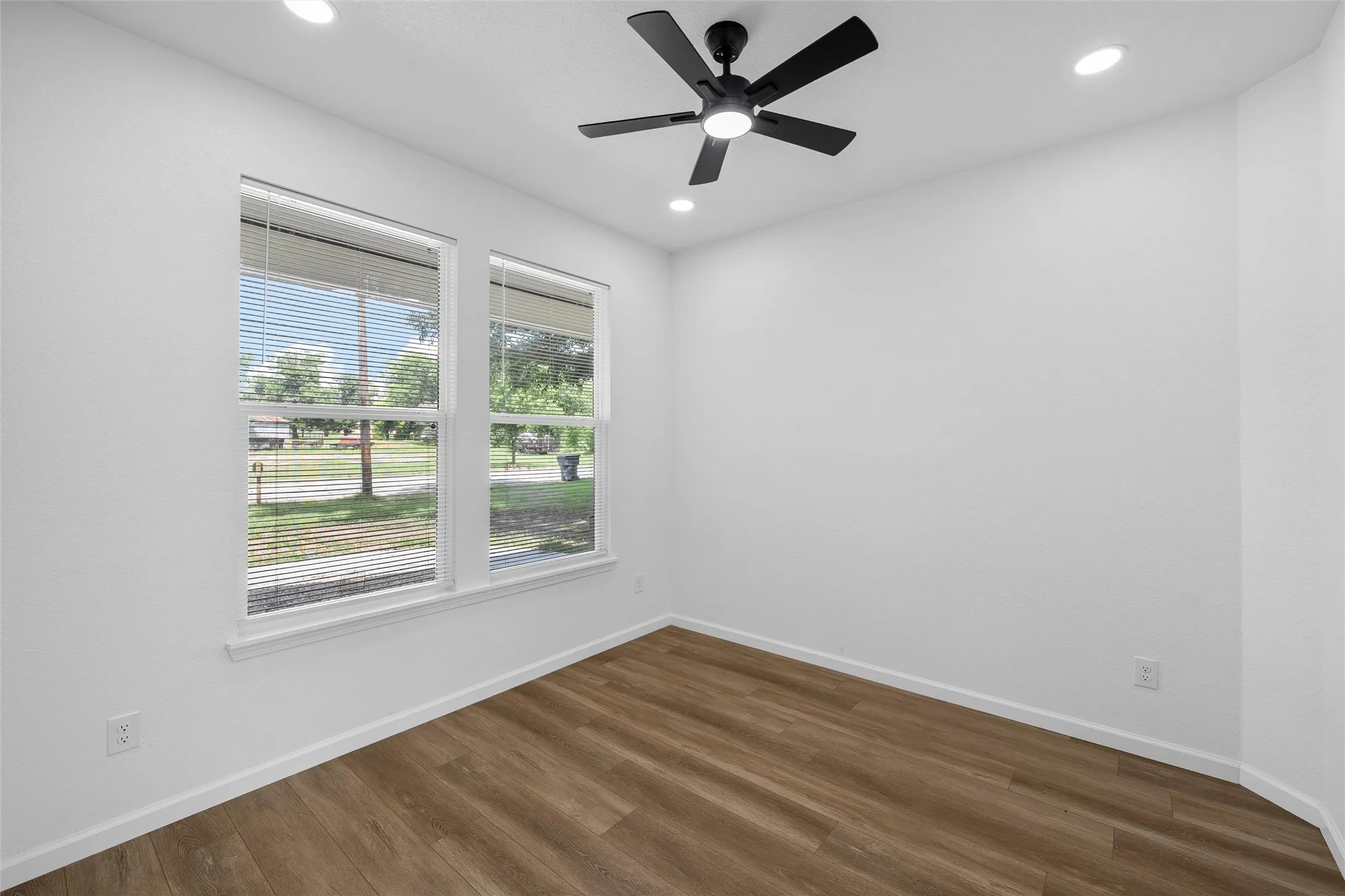 Room featuring wood-finish flooring, white walls, and dual windows with blinds