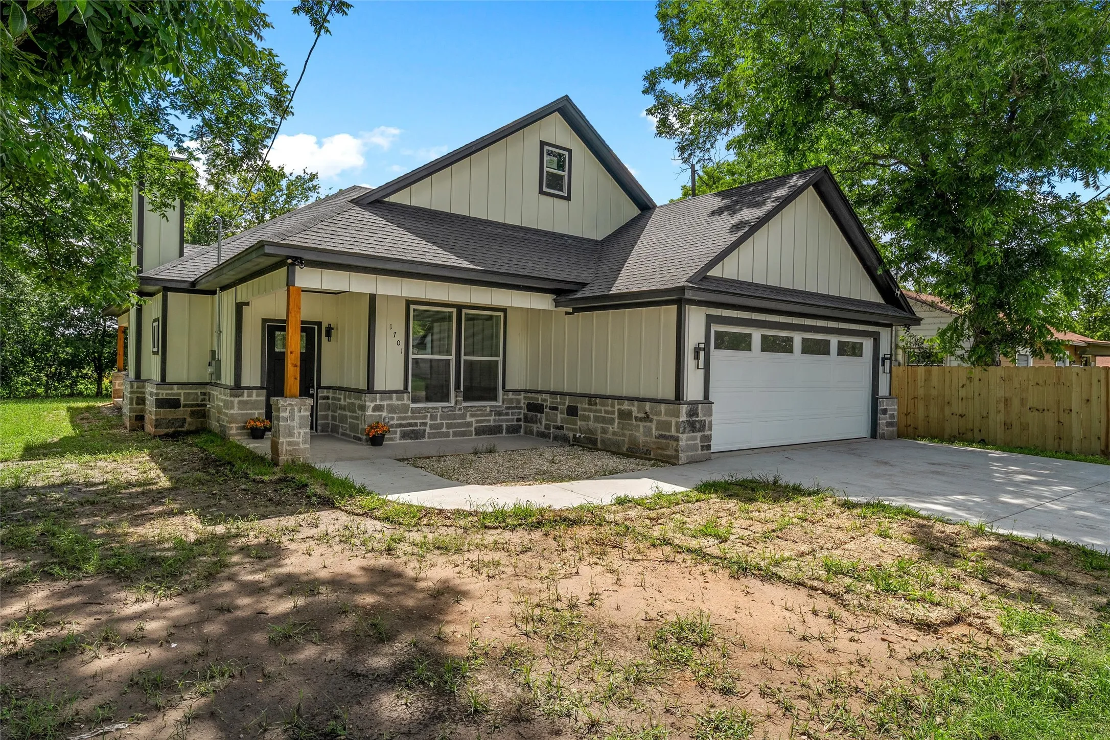 Contemporary facade featuring board and batten siding, stone veneer accents, an attached garage, a covered entry porch with a wood column, and a concrete driveway