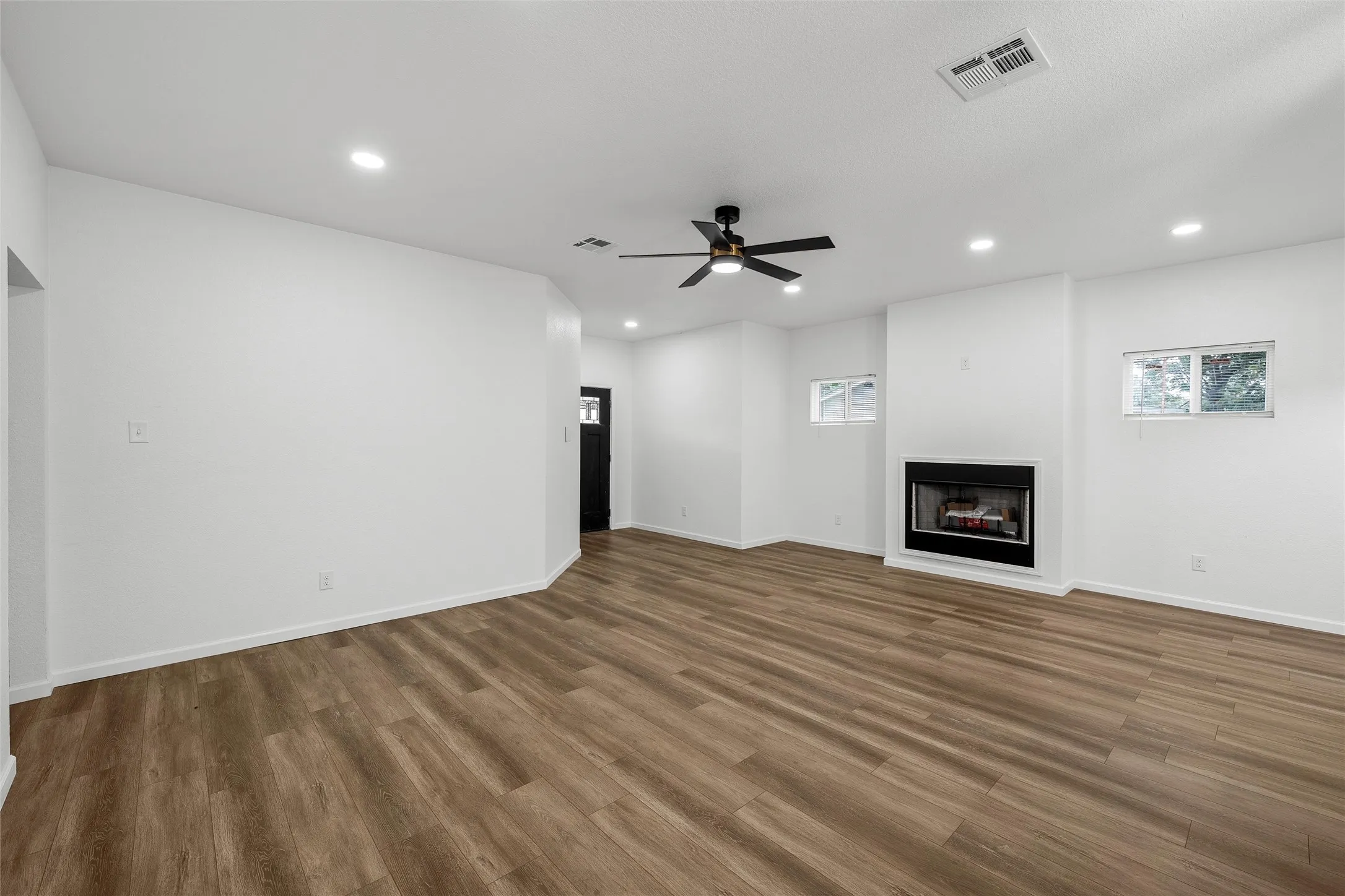 Spacious room featuring wood-finish flooring, a built-in fireplace with a white mantel, two windows, recessed lighting, and a ceiling fan