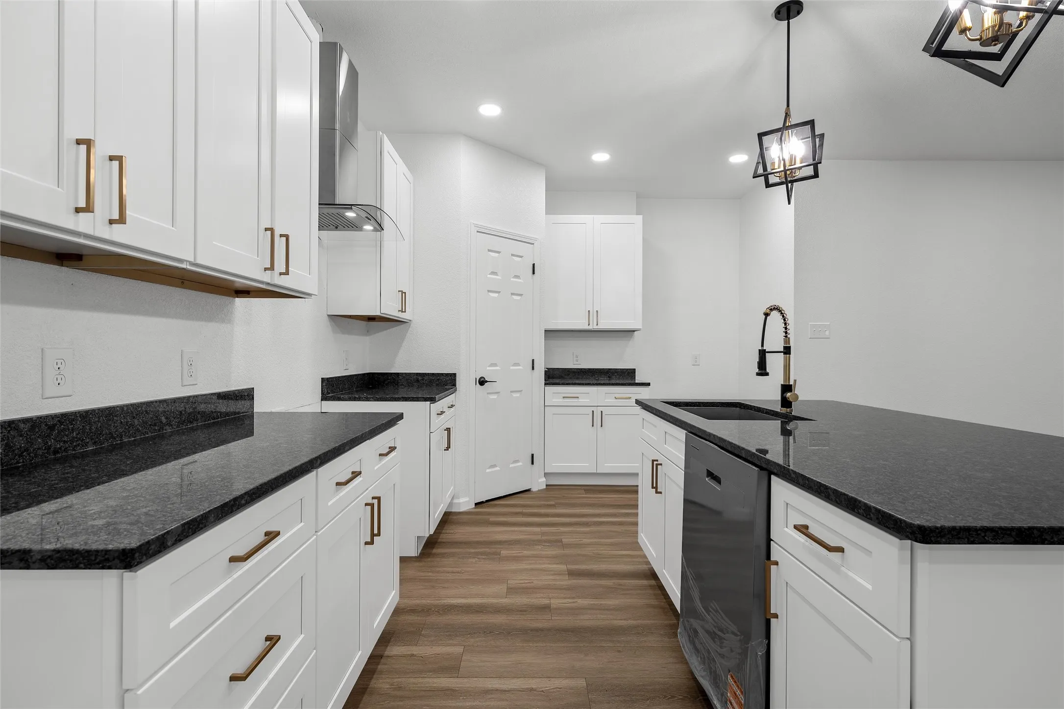 Modern kitchen featuring white shaker cabinetry with brass hardware, dark countertops, and wood-finish flooring