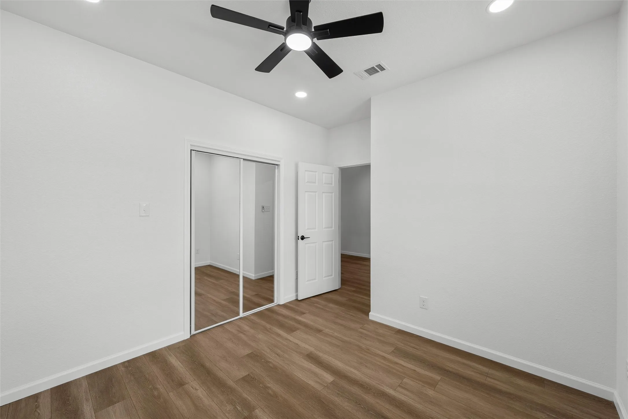 Interior room with wood-finish flooring, white walls, and a black ceiling fan with integrated lighting