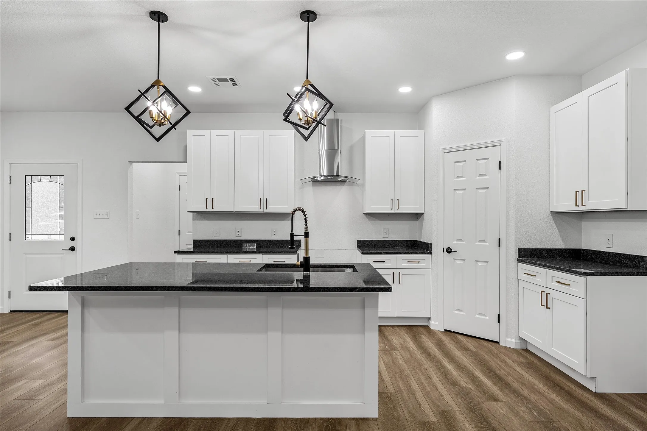 Contemporary kitchen featuring a large central island with a sink and dark countertop, white shaker-style cabinetry, stainless steel range hood, recessed lighting, and wood-finish flooring