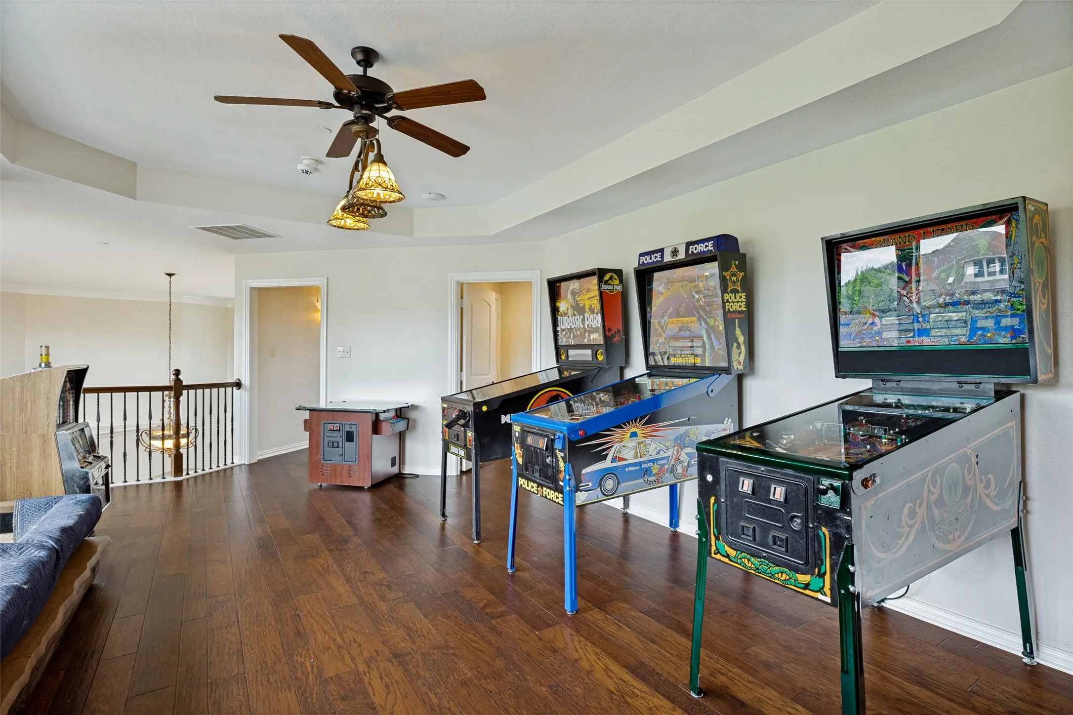Spacious upper-level room featuring wood-finish flooring, a ceiling fan with integrated lighting, and a tray ceiling detail