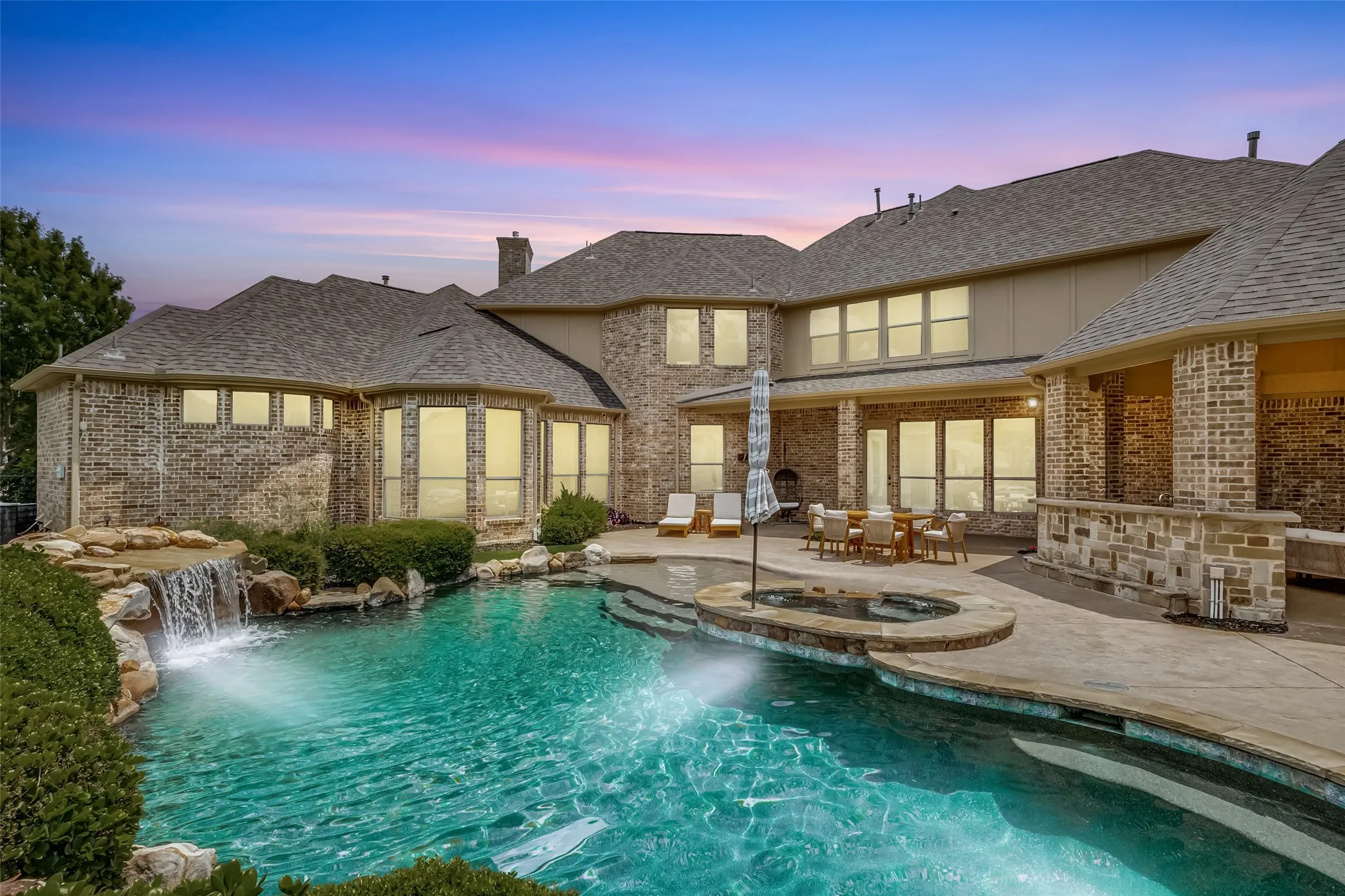Expansive outdoor living area featuring a pool with a rock waterfall, an integrated spa, a covered patio, and a built-in outdoor bar