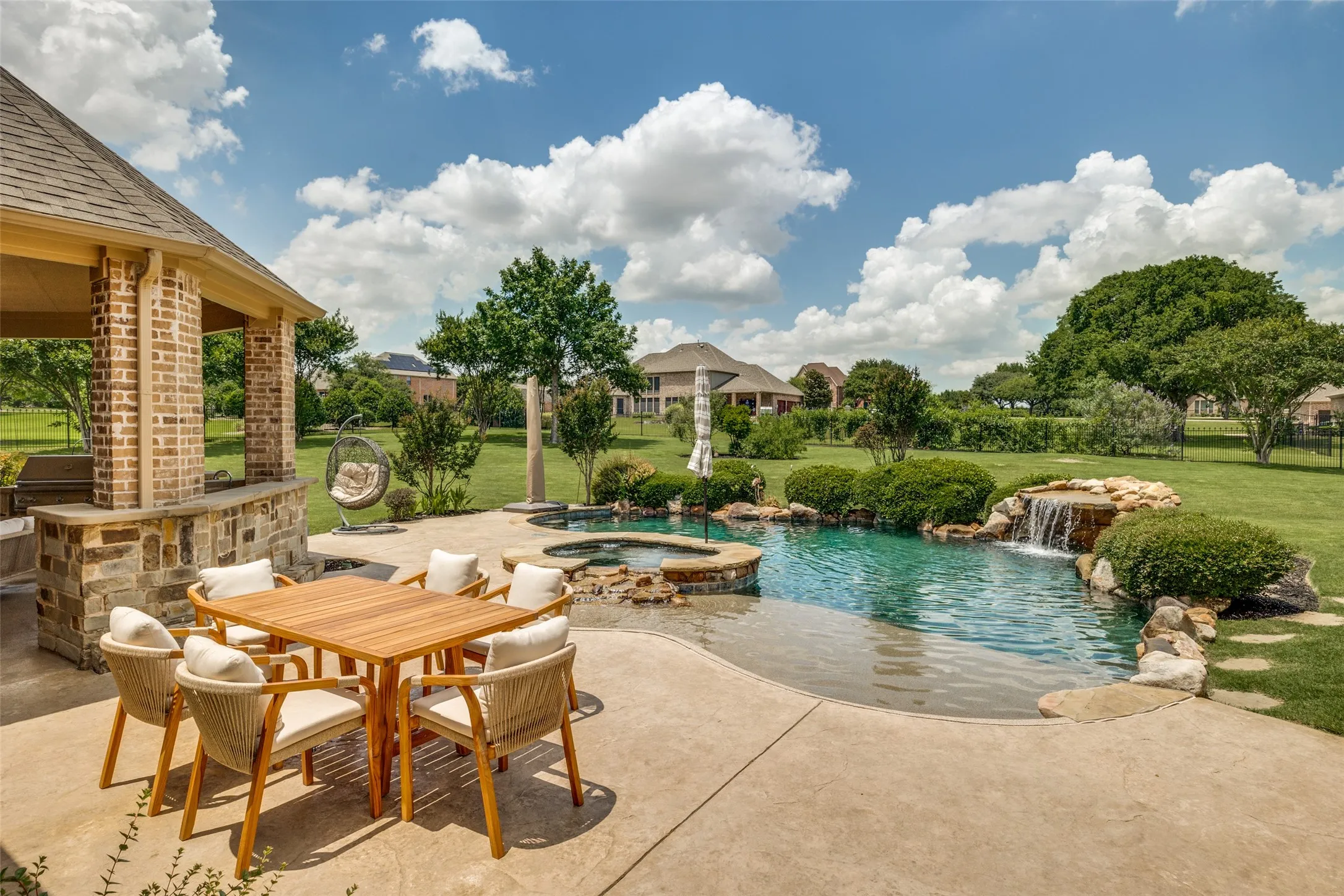 Expansive backyard oasis featuring a custom pool with a rock waterfall, an integrated spa, and a concrete patio