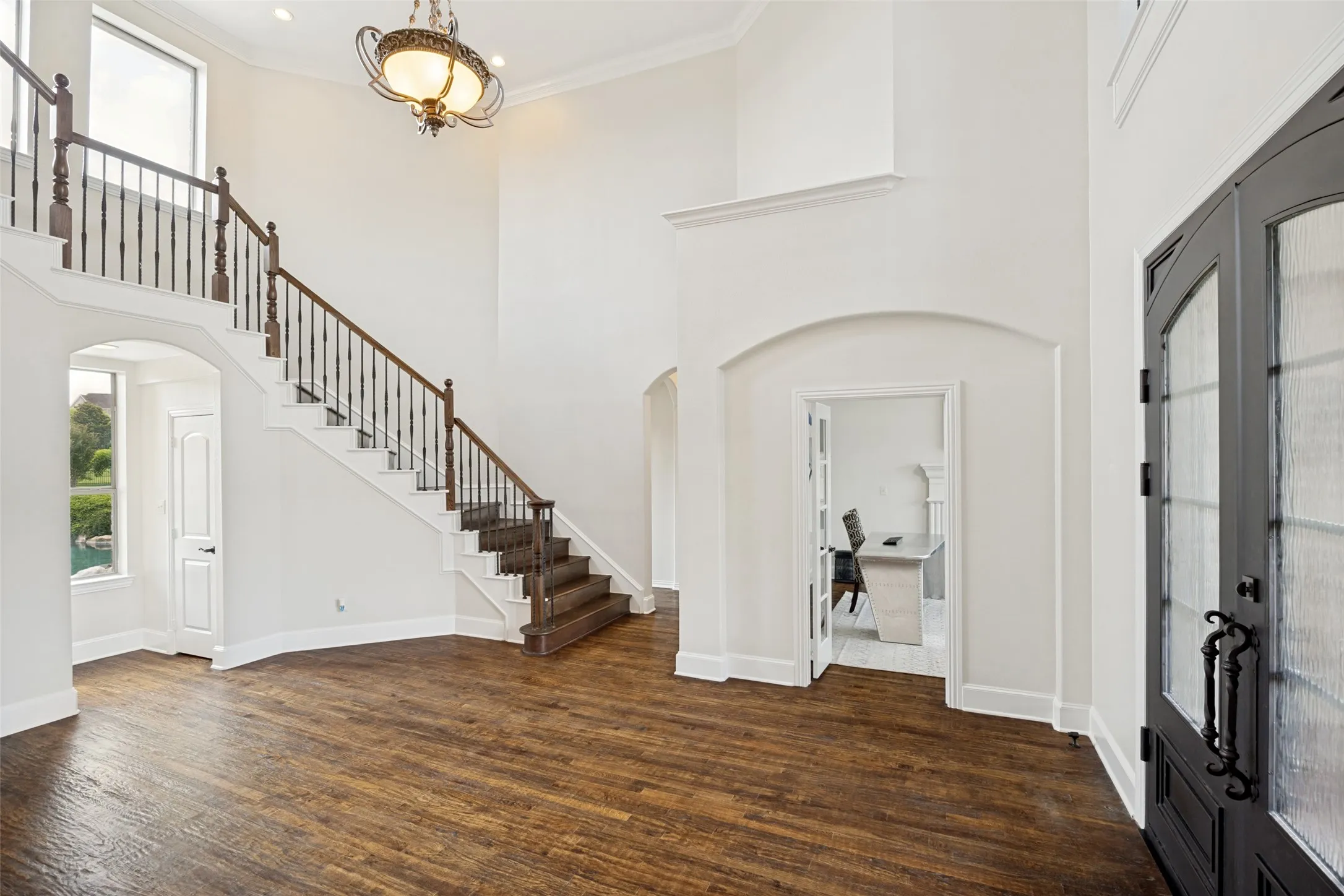 Two-story foyer featuring wood-finish flooring, a grand staircase with dark wood handrails and wrought iron balusters, and a decorative chandelier