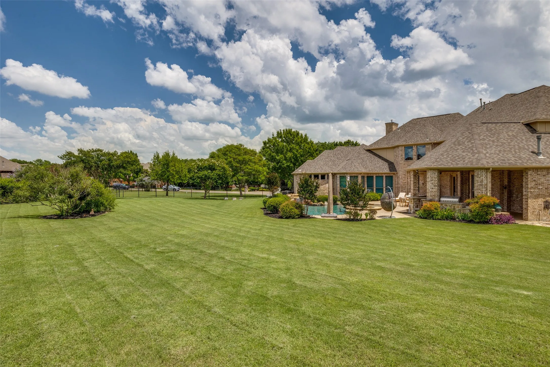 Expansive rear yard featuring a large green lawn, an in-ground pool, and a covered patio area