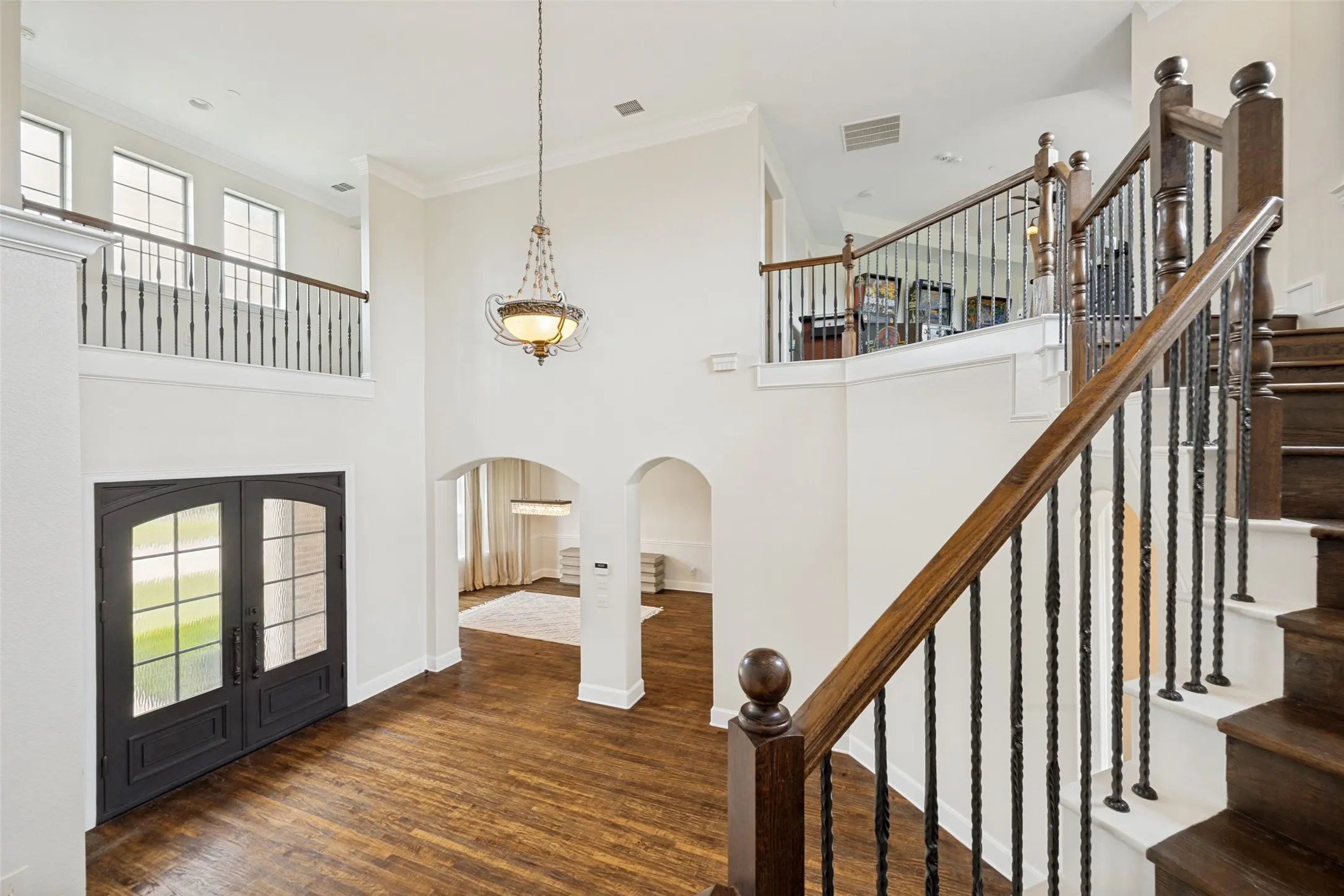 Two-story foyer with rich wood-finish flooring, a grand staircase featuring dark wood newel posts and wrought iron balusters, and a double-door entry with decorative glass panels