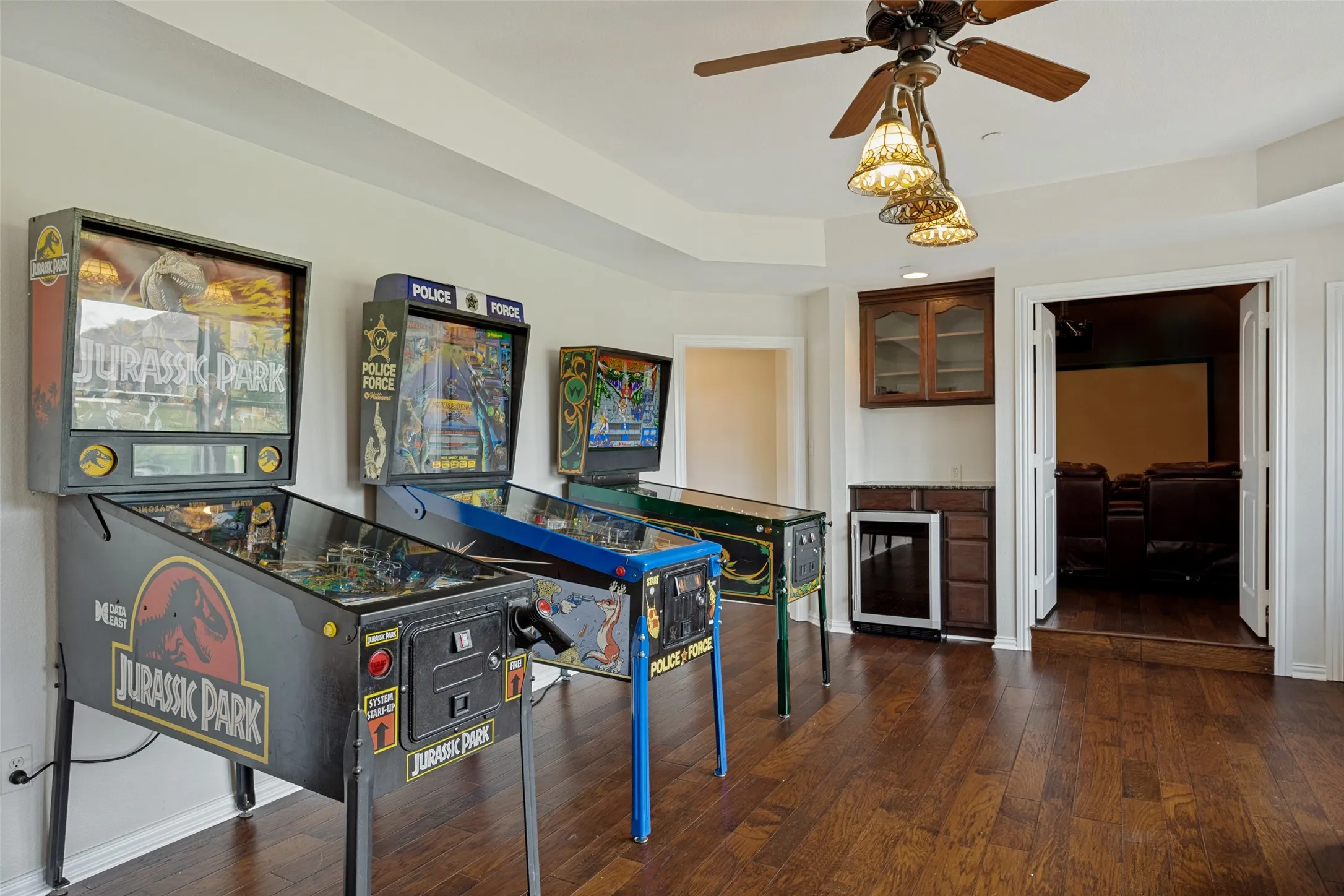 Hardwood flooring extends throughout this room, featuring a built-in wet bar with cabinetry, stone countertop, and beverage refrigerator