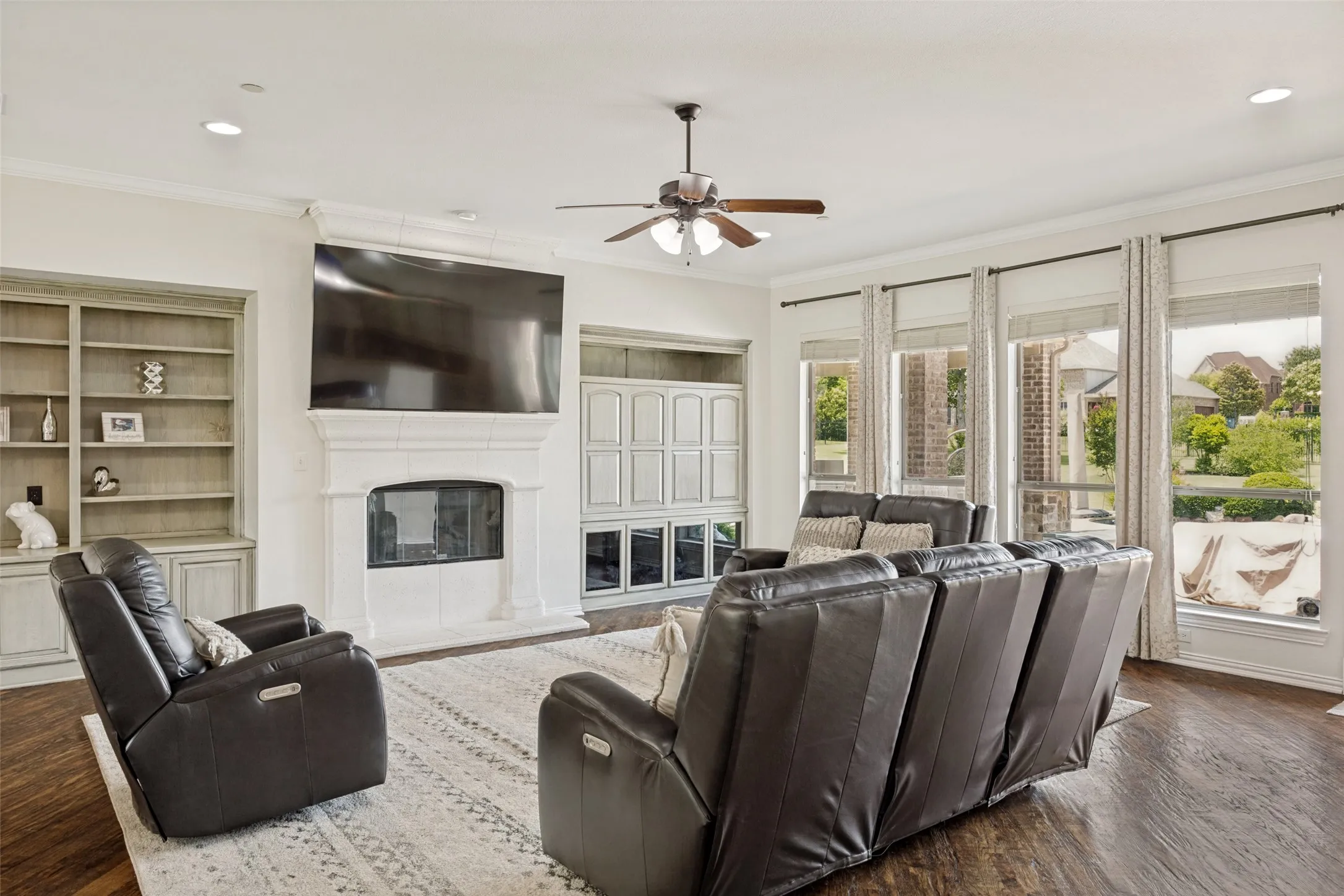 Spacious living area featuring a stone-clad fireplace, integrated media built-ins, wood-finish flooring, recessed lighting, and expansive windows