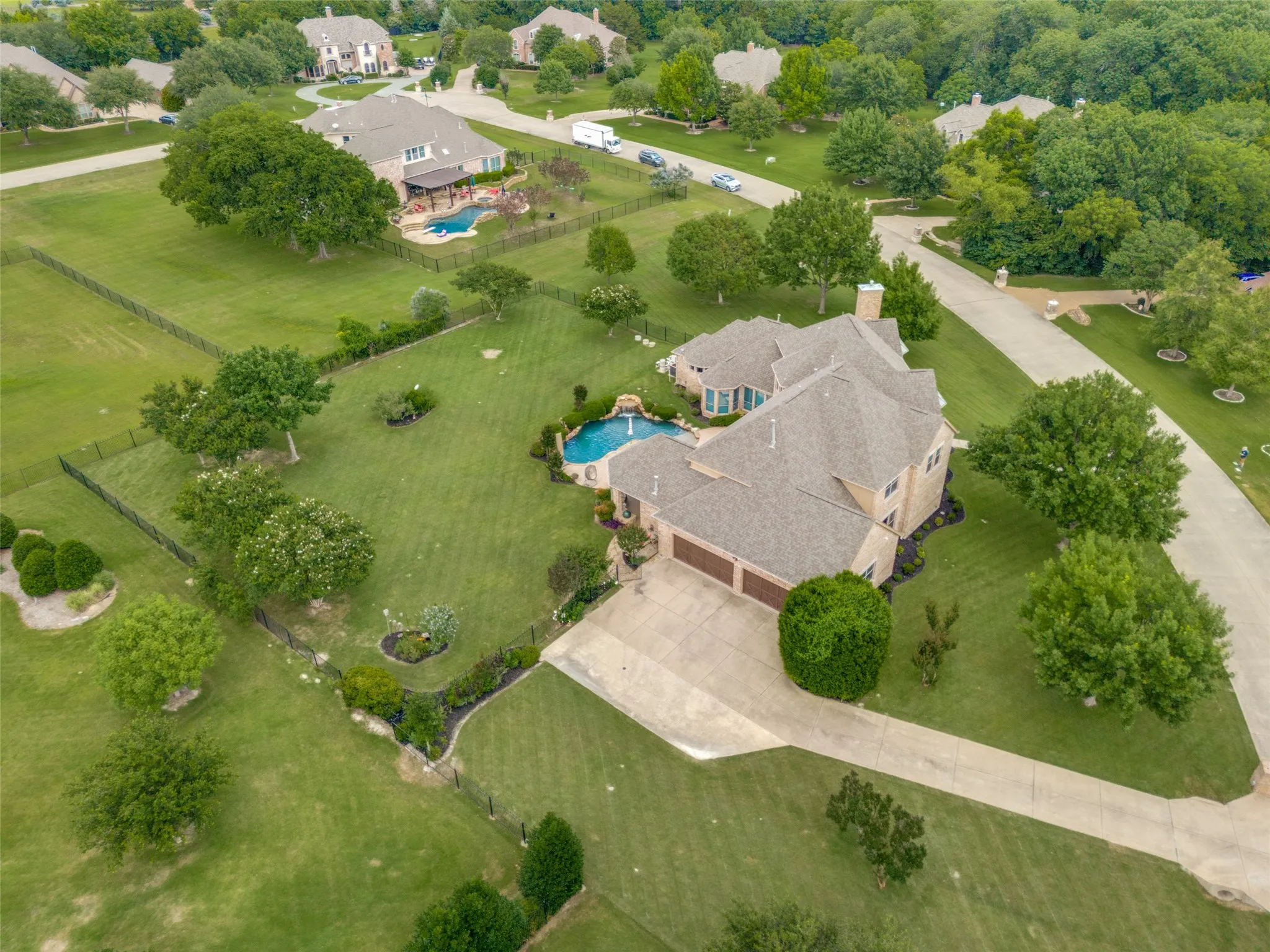 Spacious property featuring a large residence, a multi-car garage, a meandering driveway, mature trees, and a sculpted backyard swimming pool with an integrated spa