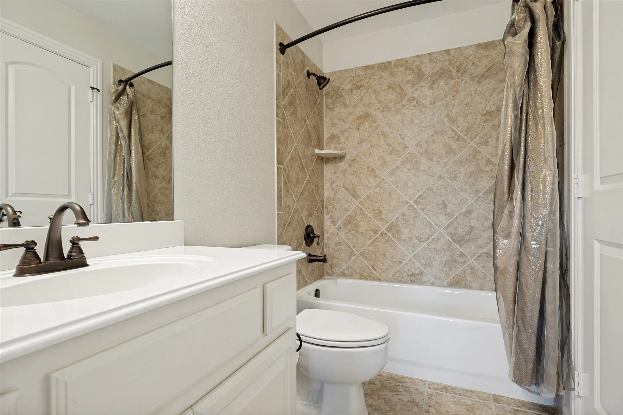 Bathroom featuring a white vanity with integrated sink, bronze faucet, and a shower-tub combination with diagonal tile surround
