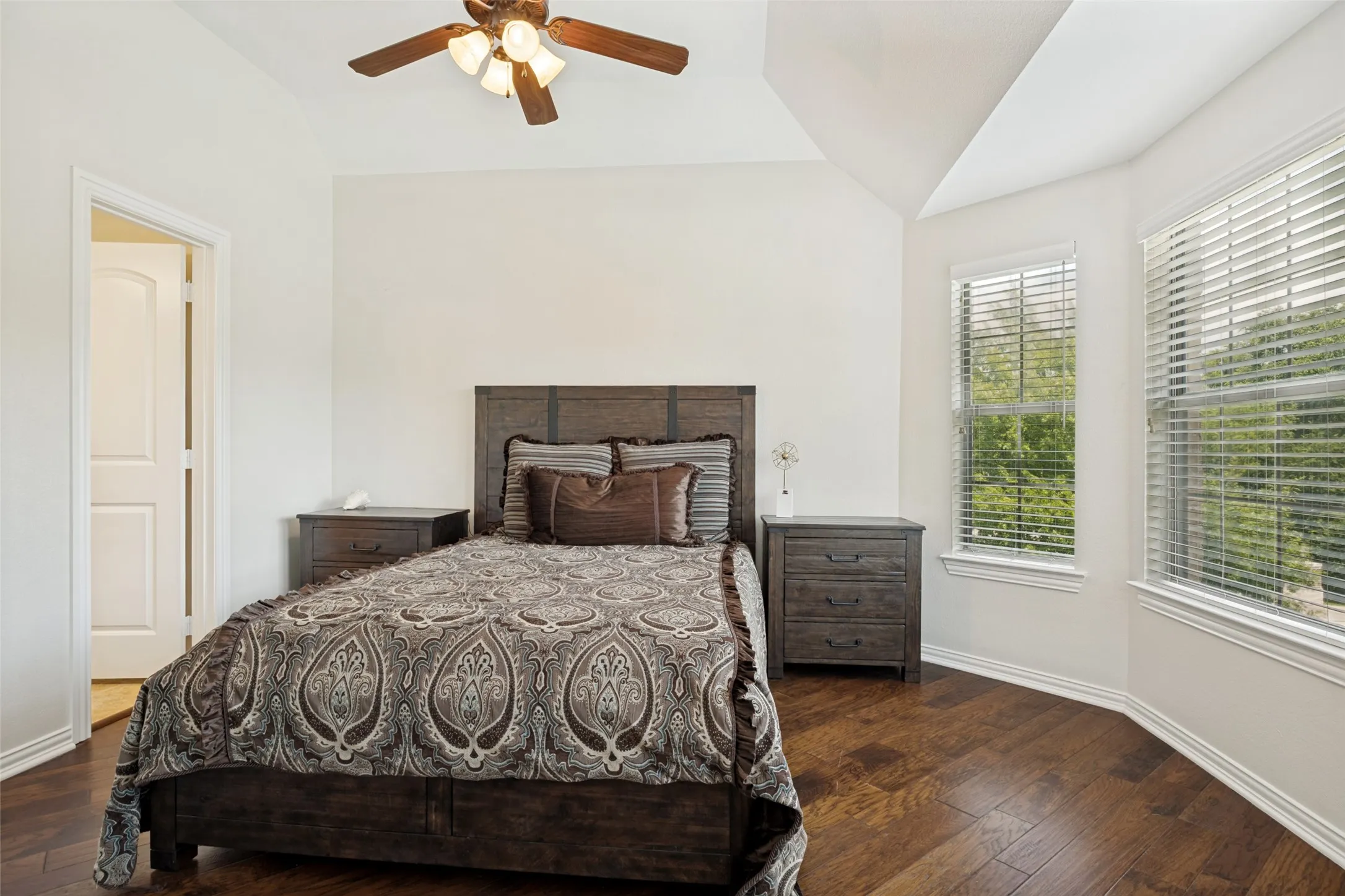 Bright room featuring wood-finish flooring, a tray ceiling, and a ceiling fan with integrated lighting