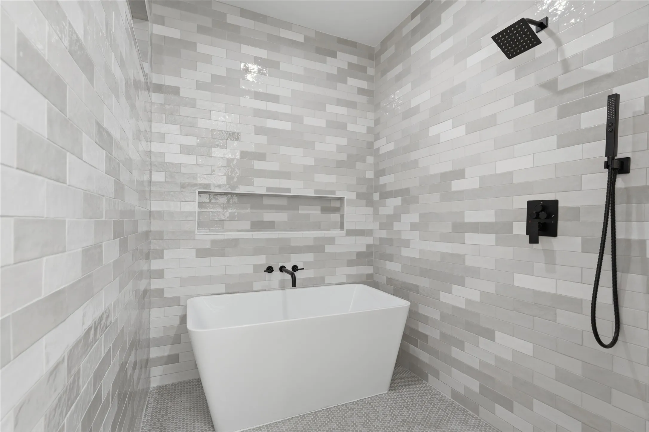 Freestanding soaking tub set against a tiled wall with a recessed niche