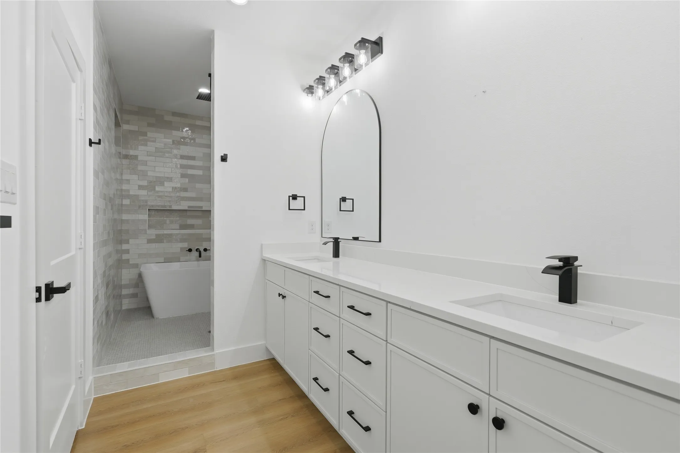 Spacious bathroom with dual vanities featuring white cabinetry, integrated sinks, and matte black fixtures