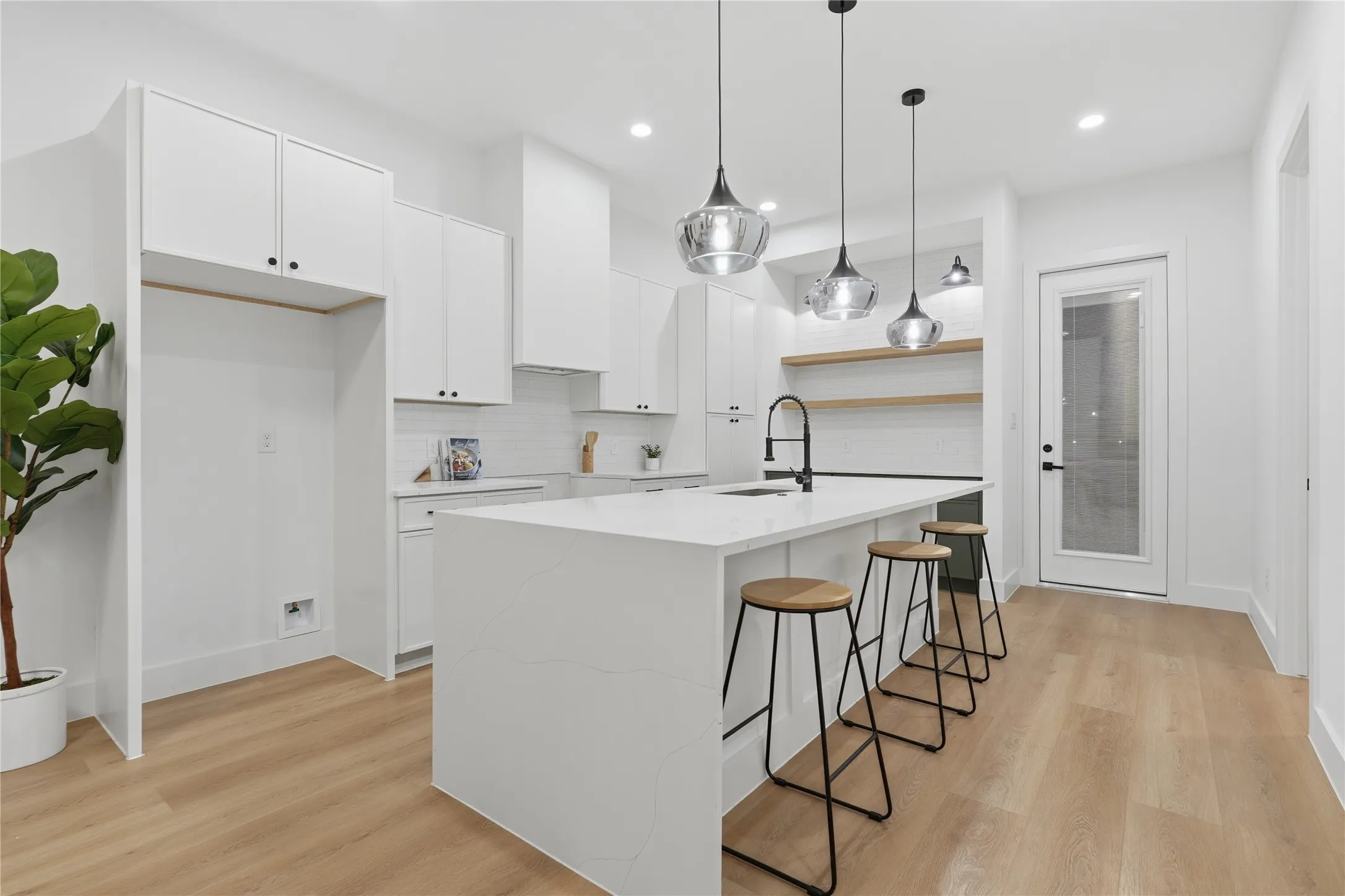 Contemporary kitchen featuring a large waterfall-edge island with seating, white shaker cabinetry, and wood-finish flooring