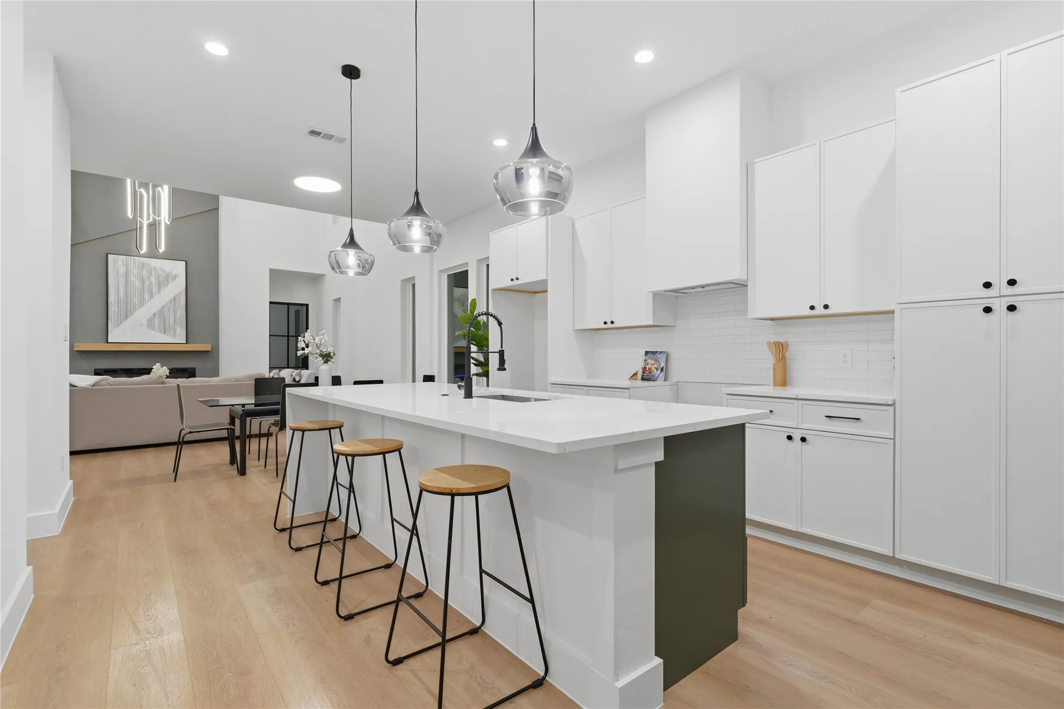 Open-concept kitchen featuring an oversized island with seating, white shaker cabinetry, white subway tile backsplash, and wood-finish flooring
