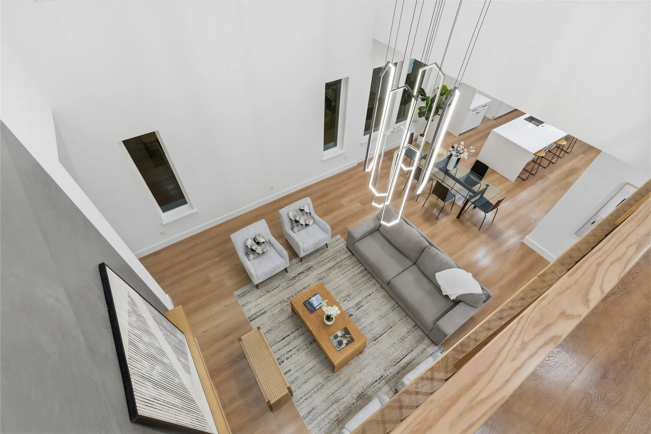 Double-height living space featuring wood-finish flooring, a contemporary linear chandelier, and recessed windows