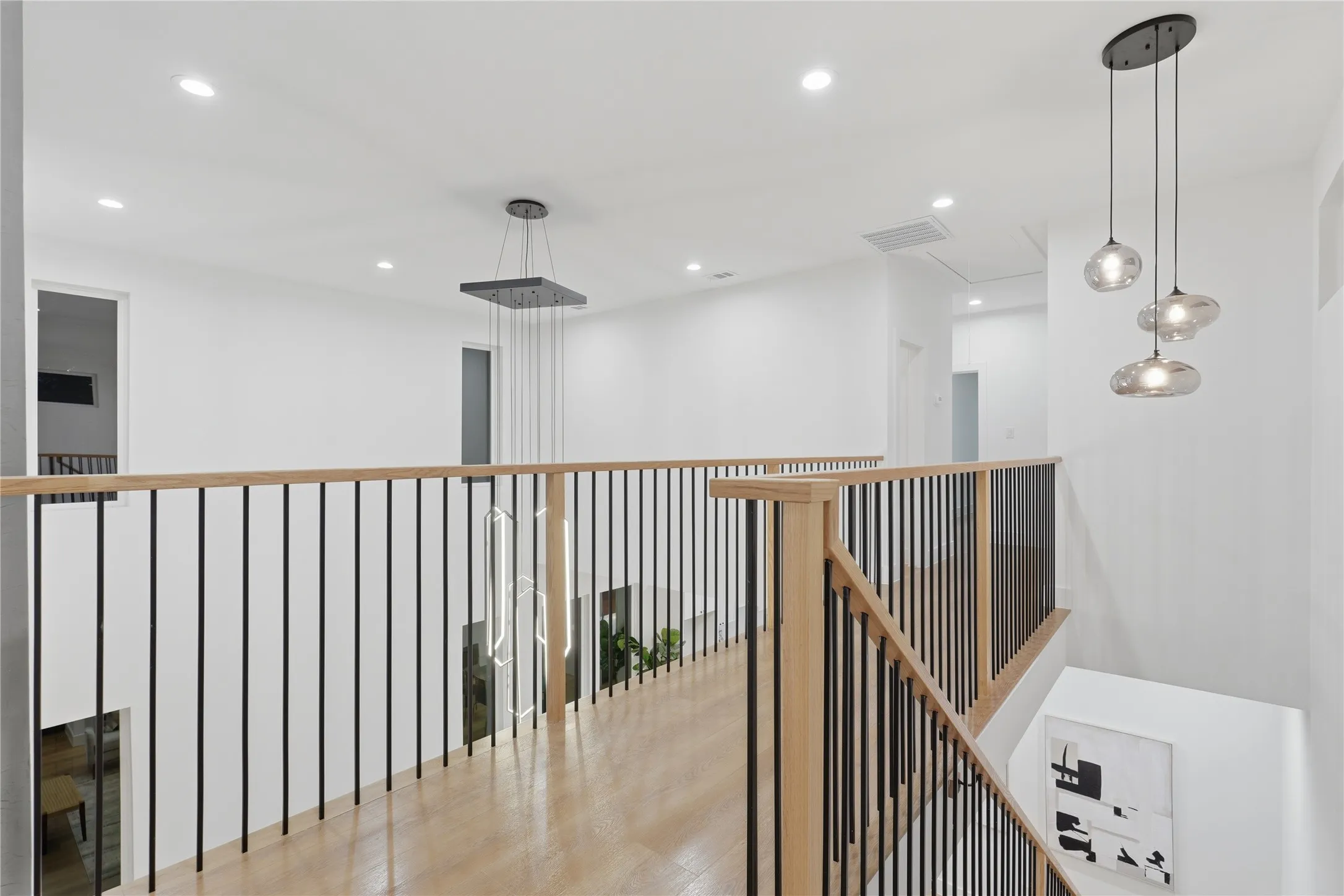 Upper-level hallway featuring wood-finish flooring, light wood handrails with black metal balusters, and recessed lighting