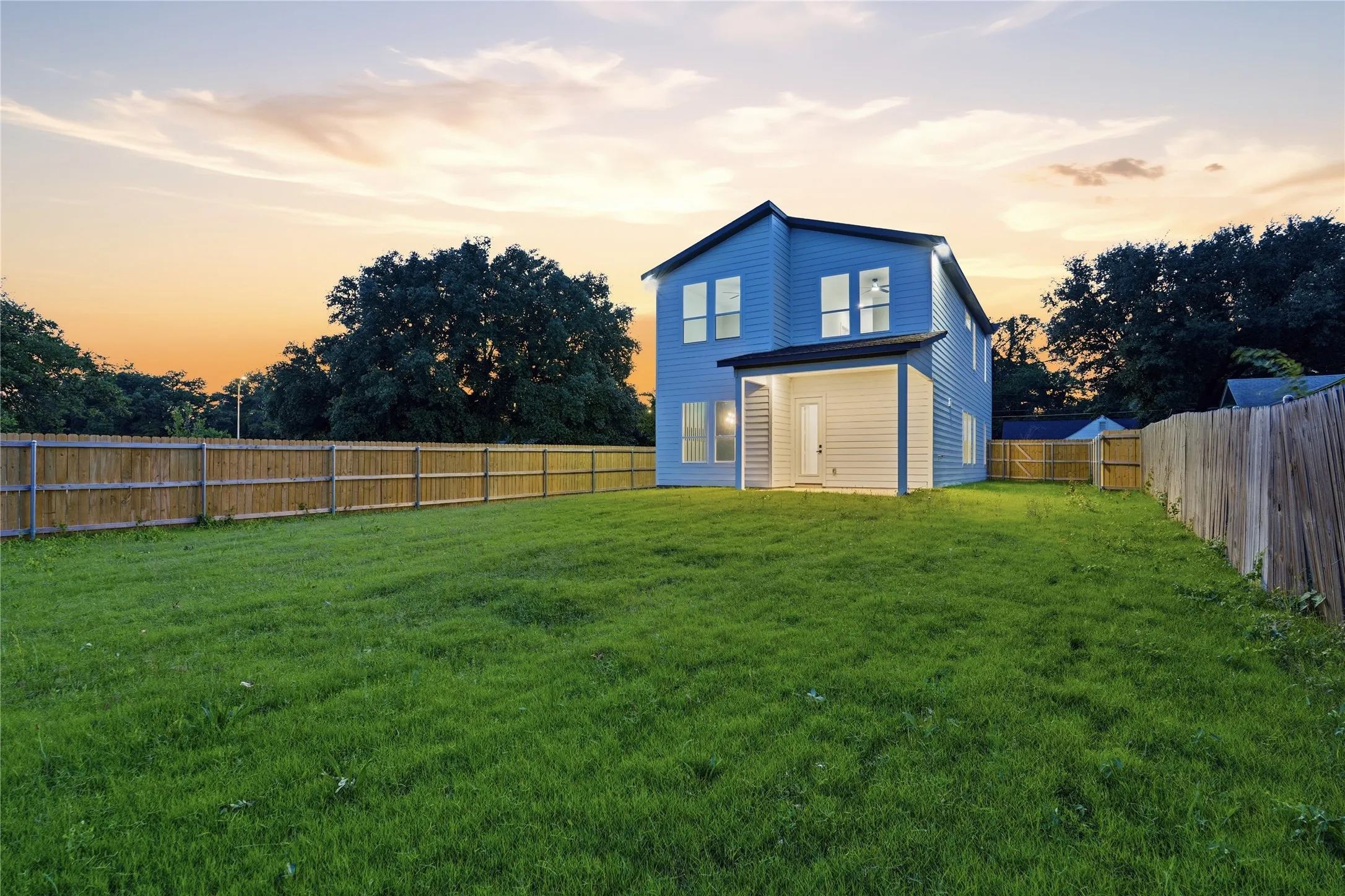 Expansive backyard featuring a large green lawn, full perimeter privacy fencing, and a covered patio area