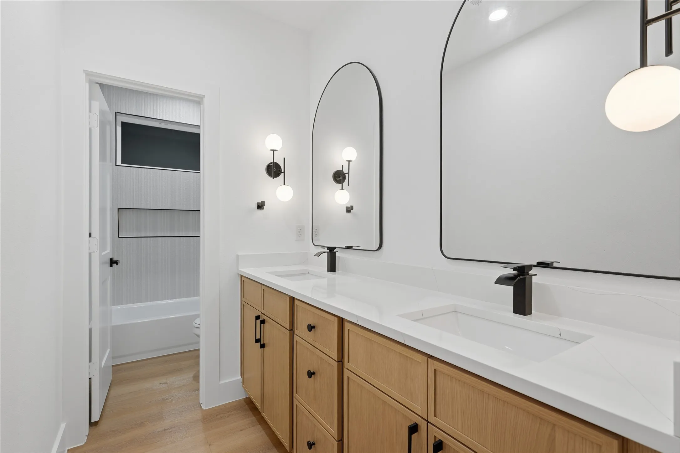 Dual vanity with light wood-finish cabinetry, white countertops, and integrated rectangular sinks