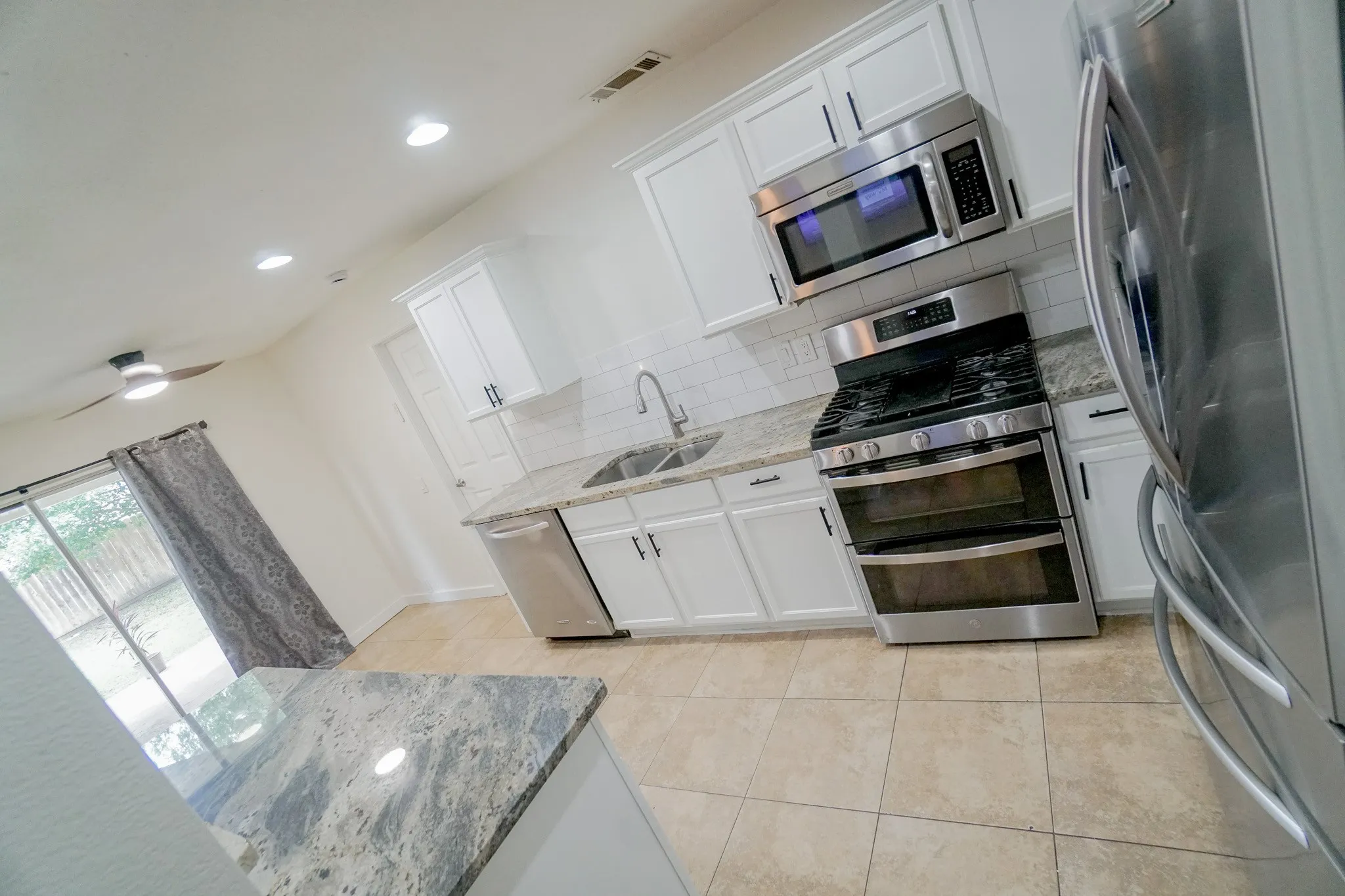 Contemporary kitchen featuring white cabinetry, stone countertops, stainless steel appliances, a subway tile backsplash, and ceramic tile flooring