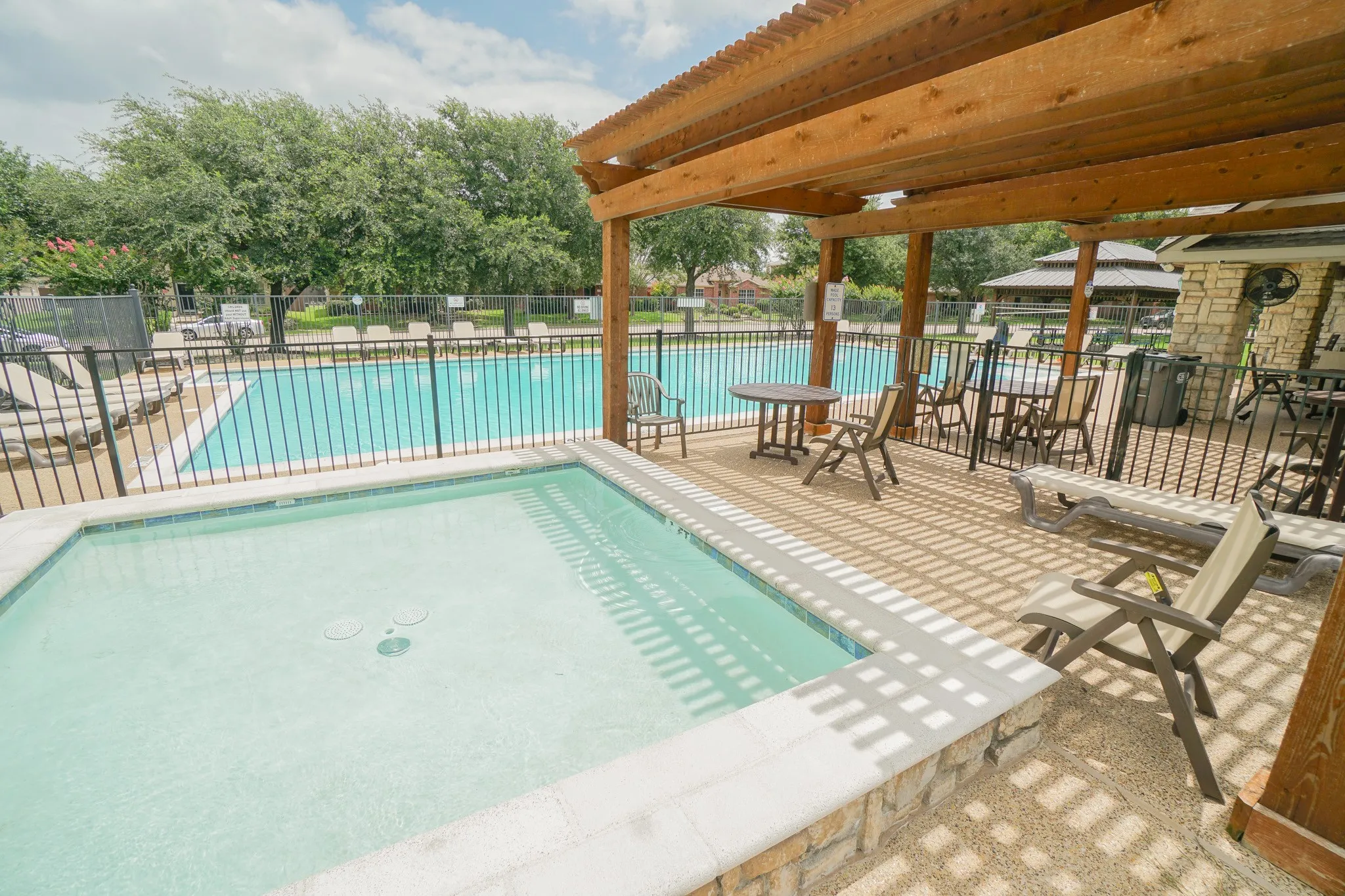 Community Pool and spa with a surrounding patio featuring a pergola, stone accents, and a nearby swimming pool