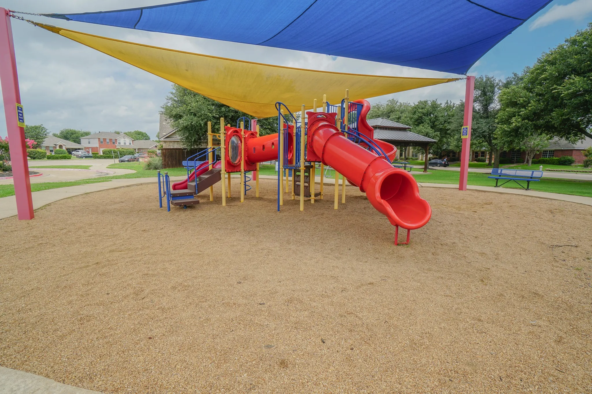 Community playground featuring a red and blue play structure with slides and tunnels