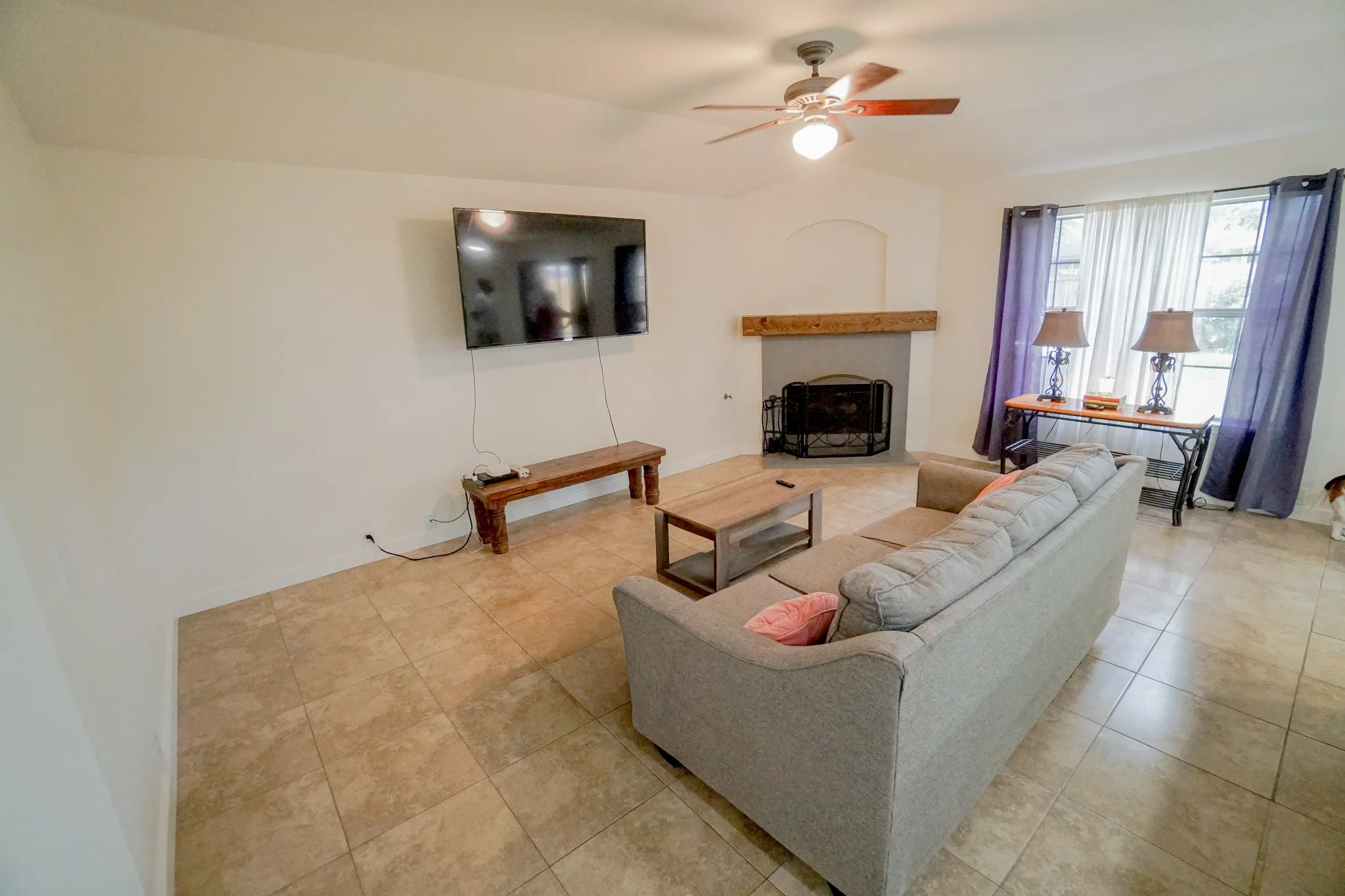 Bright interior space featuring a ceiling fan with integrated lighting, a fireplace with a wood mantel, tiled flooring, and multiple windows
