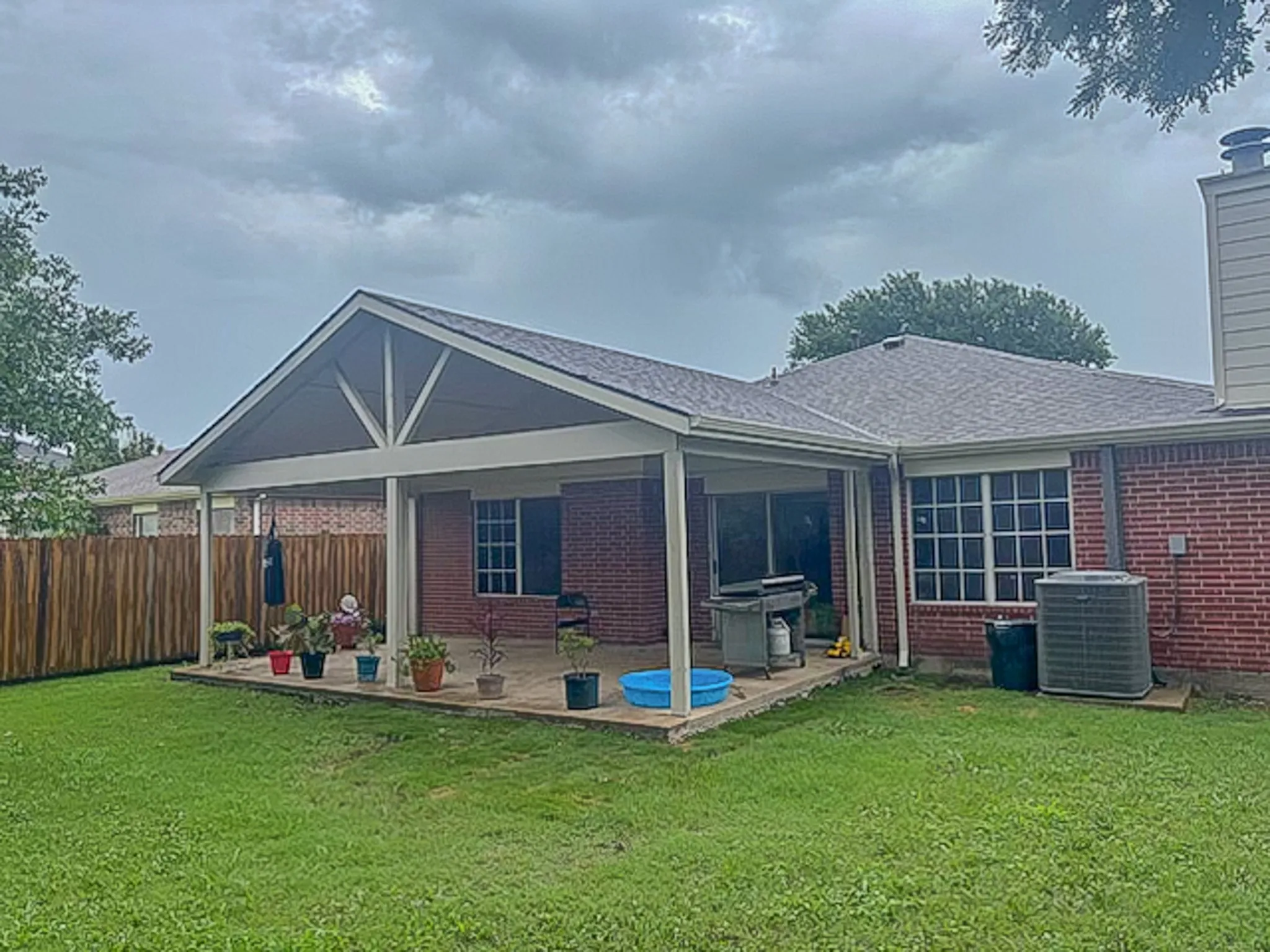 Expansive backyard featuring a covered patio, brick exterior, and a new privacy fence