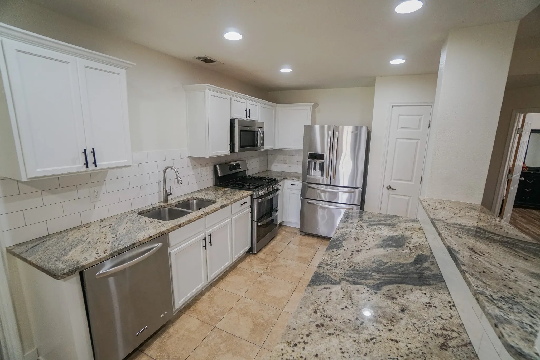 Kitchen featuring white cabinetry with dark hardware, a subway tile backsplash, stainless steel appliances, and granite countertops