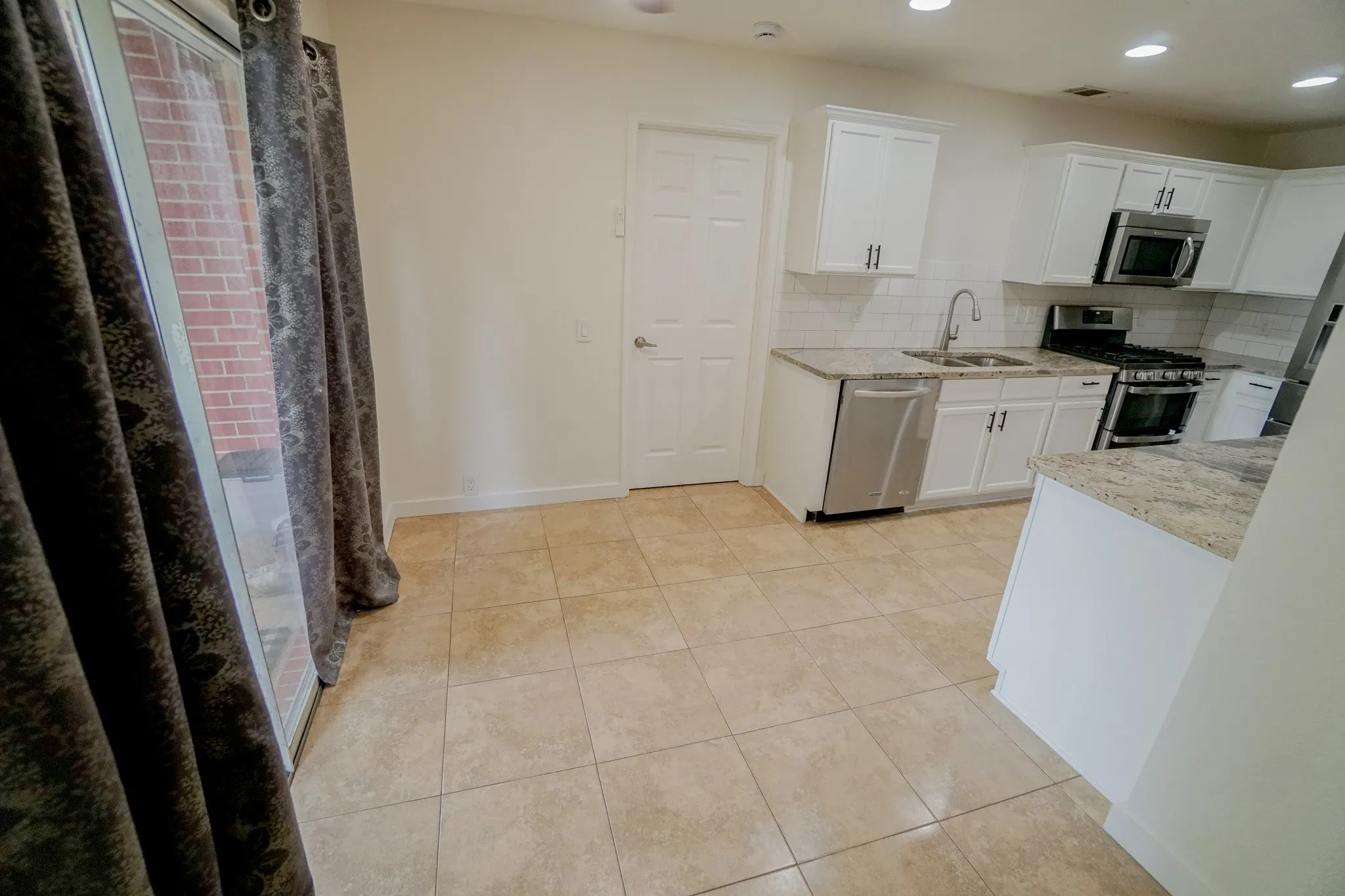 Kitchen featuring white cabinetry, light granite countertops, a subway tile backsplash, stainless steel appliances, and tile flooring