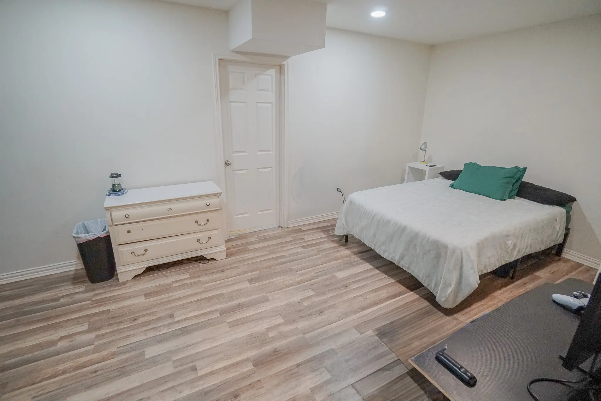 Spacious room featuring wood-finish flooring, white walls, recessed lighting, and a paneled interior door