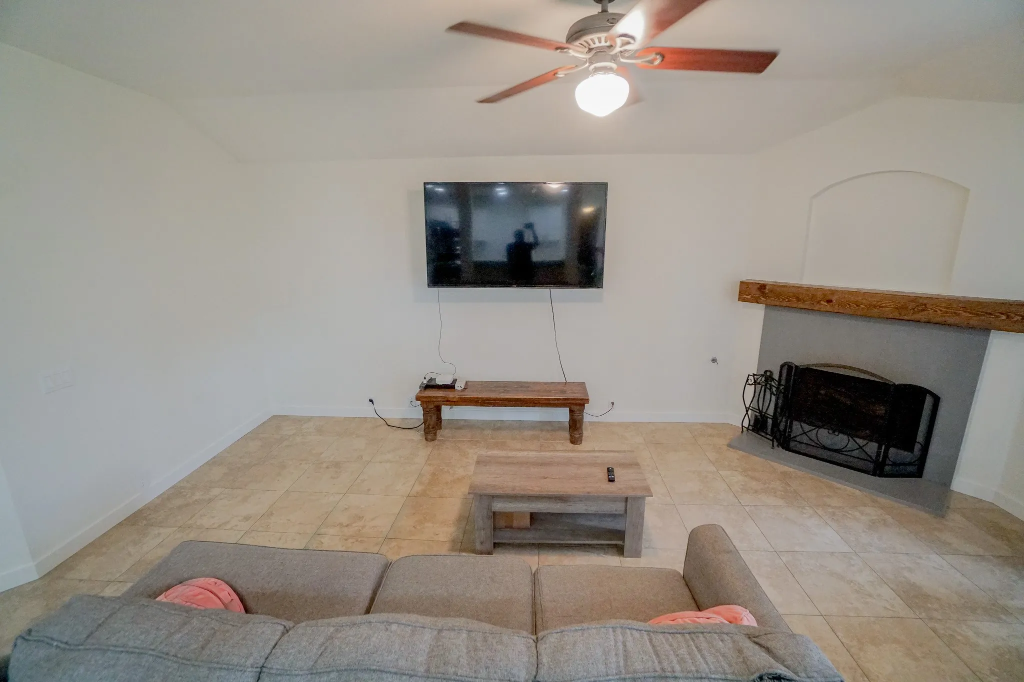 Spacious living area featuring tile flooring, a ceiling fan with integrated lighting, and an arched fireplace with a substantial wood mantel