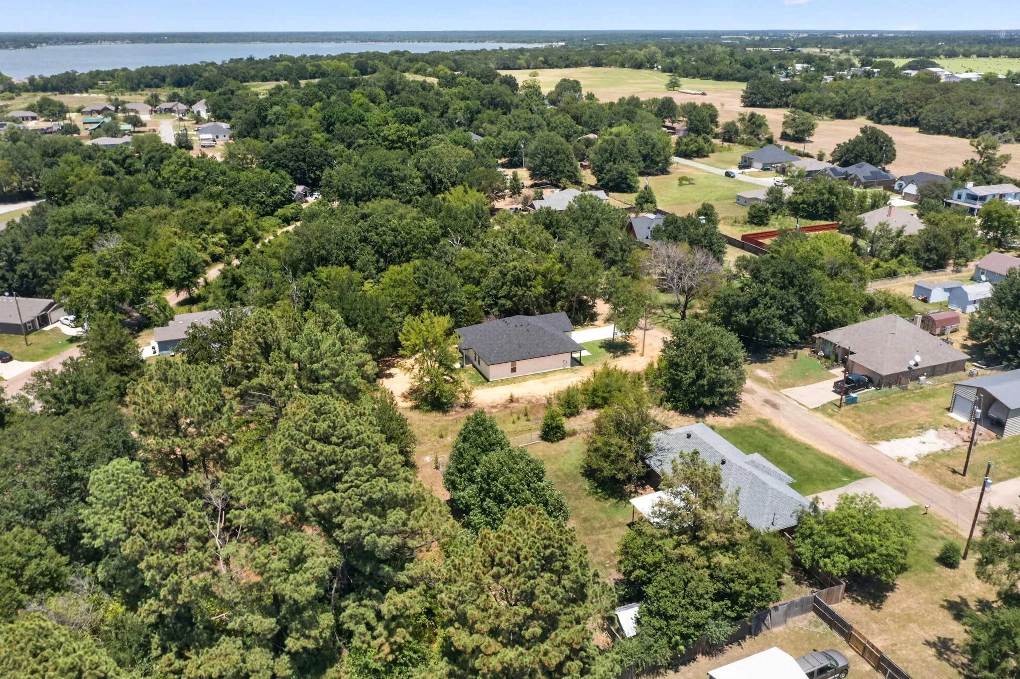 Aerial perspective showcasing a residential area bordered by a large body of water, extensive tree coverage, and open fields