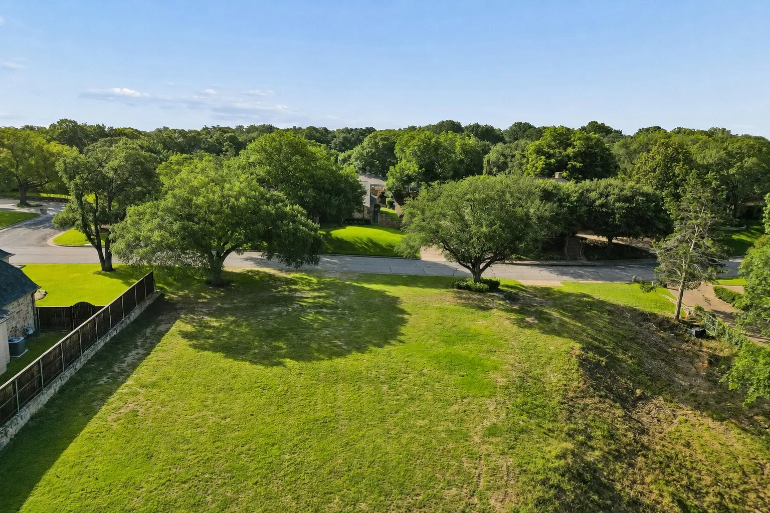 Aerial view over the open/prepped build area, highlighting street frontage, mature trees, and the lot’s elevated setting.