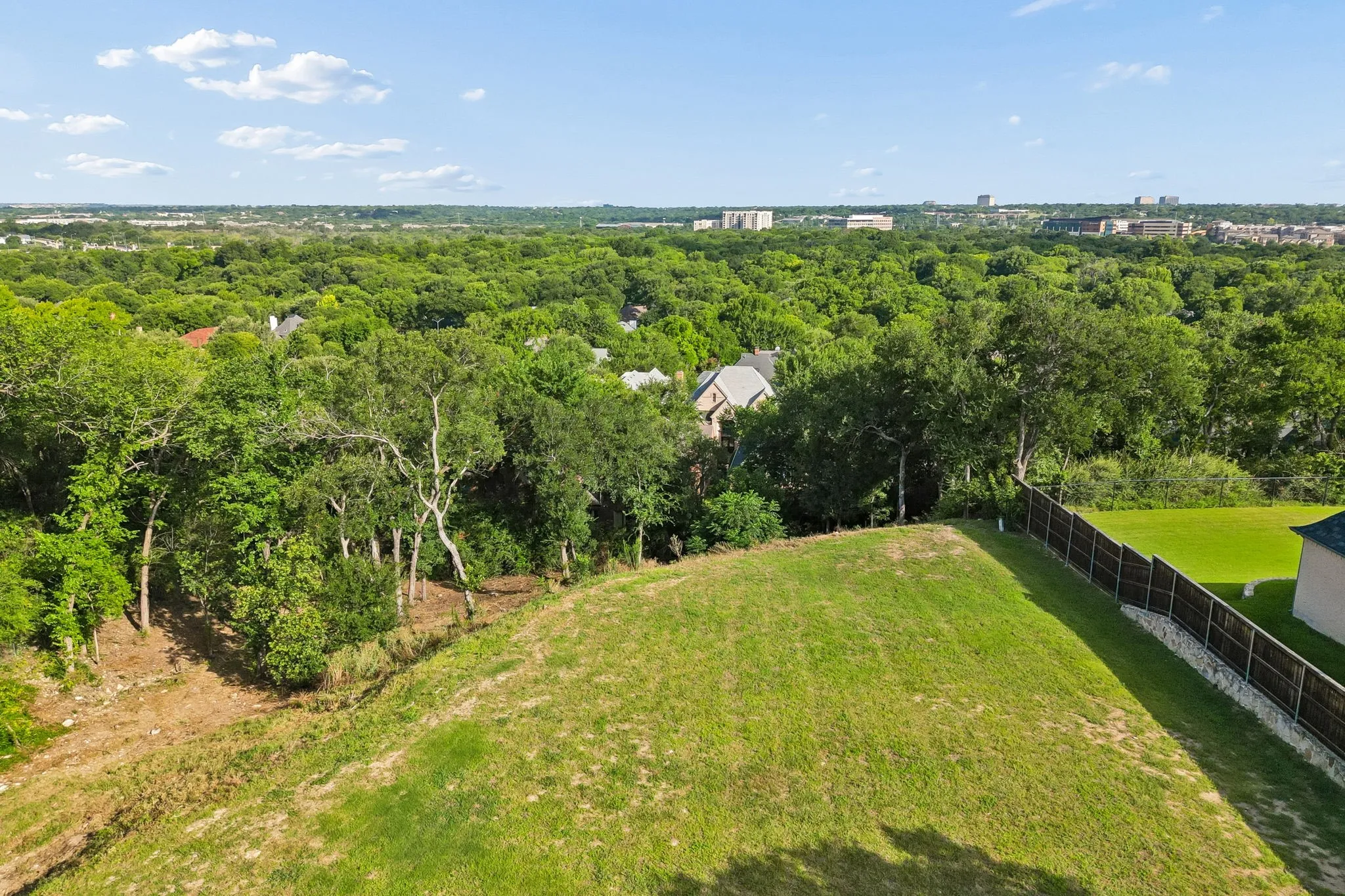 Aerial perspective looking across the homesite toward mature trees, nearby estate homes, and elevated views beyond the property.