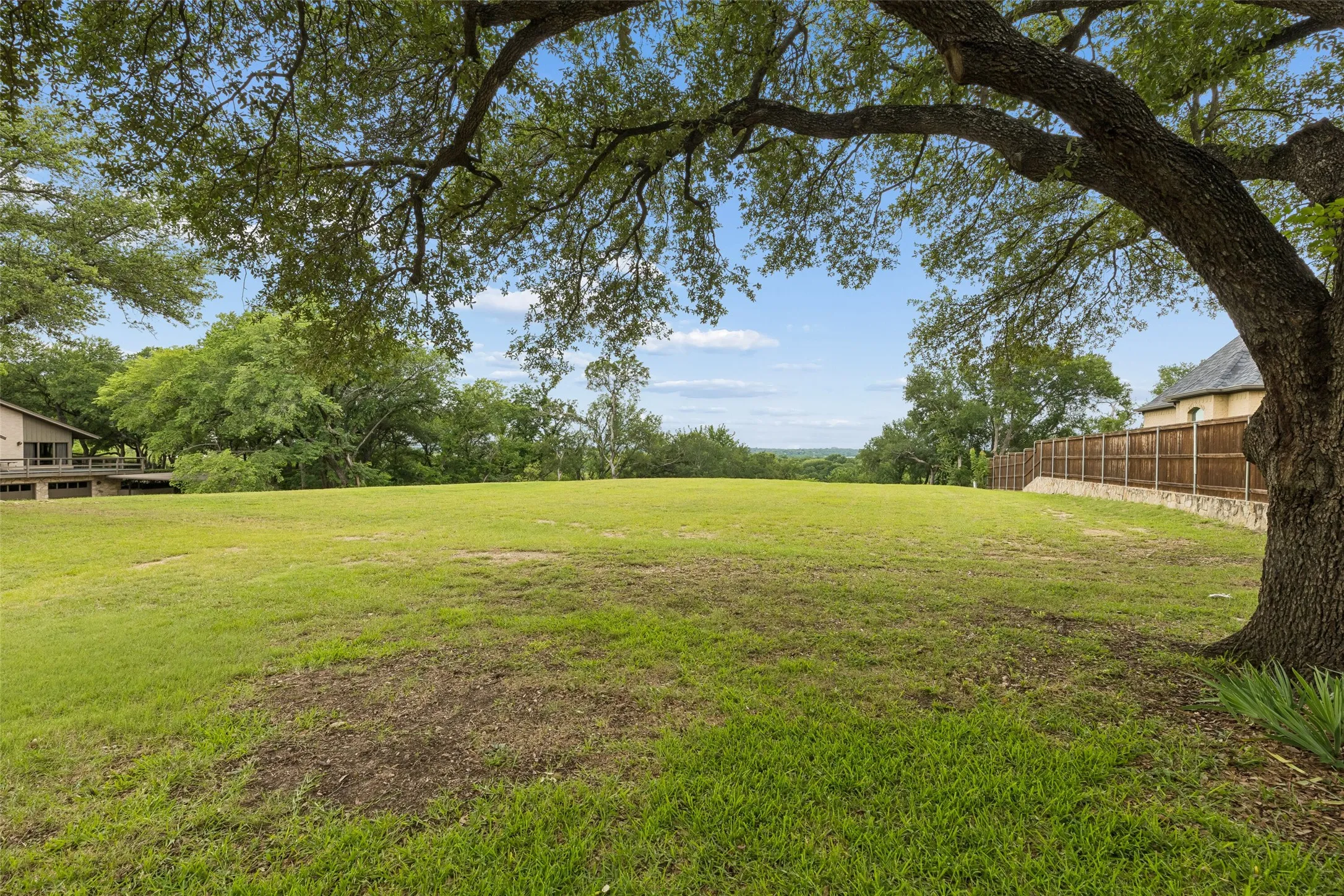 Ground-level view framed by mature trees, showing the open/prepped build area and peaceful elevated backdrop.