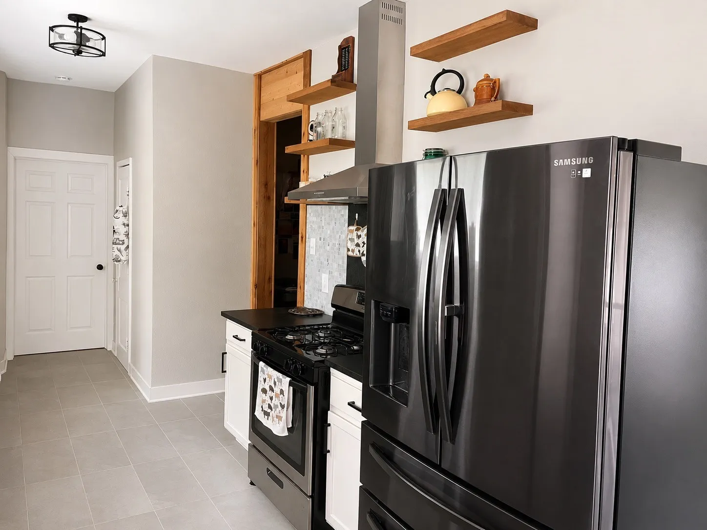 Kitchen featuring stainless steel appliances, light gray tile flooring, white cabinetry, black countertops, and open wood shelving