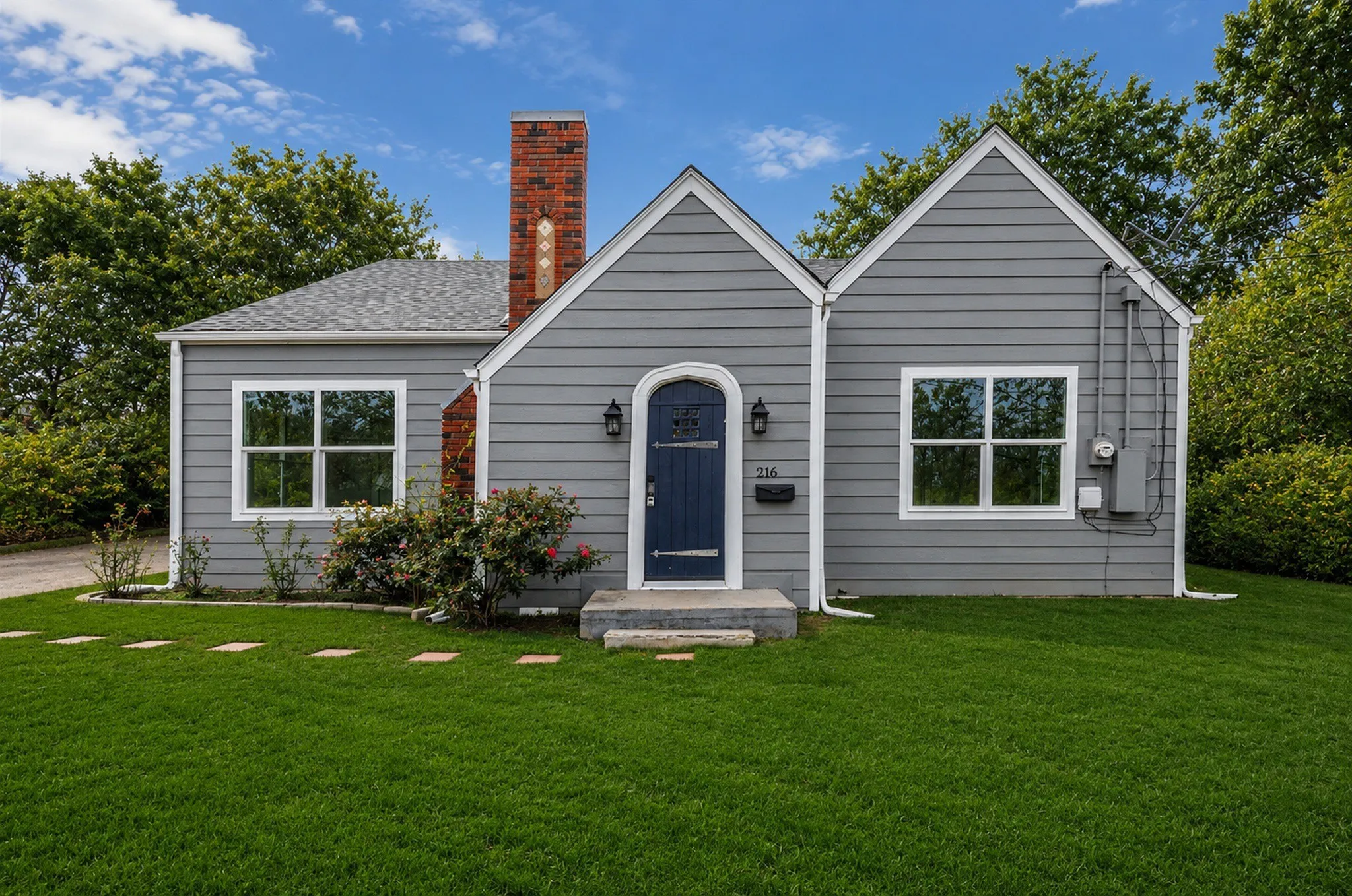 Charming exterior featuring gray horizontal siding, a prominent brick chimney with decorative detailing, and an arched navy blue entry door
