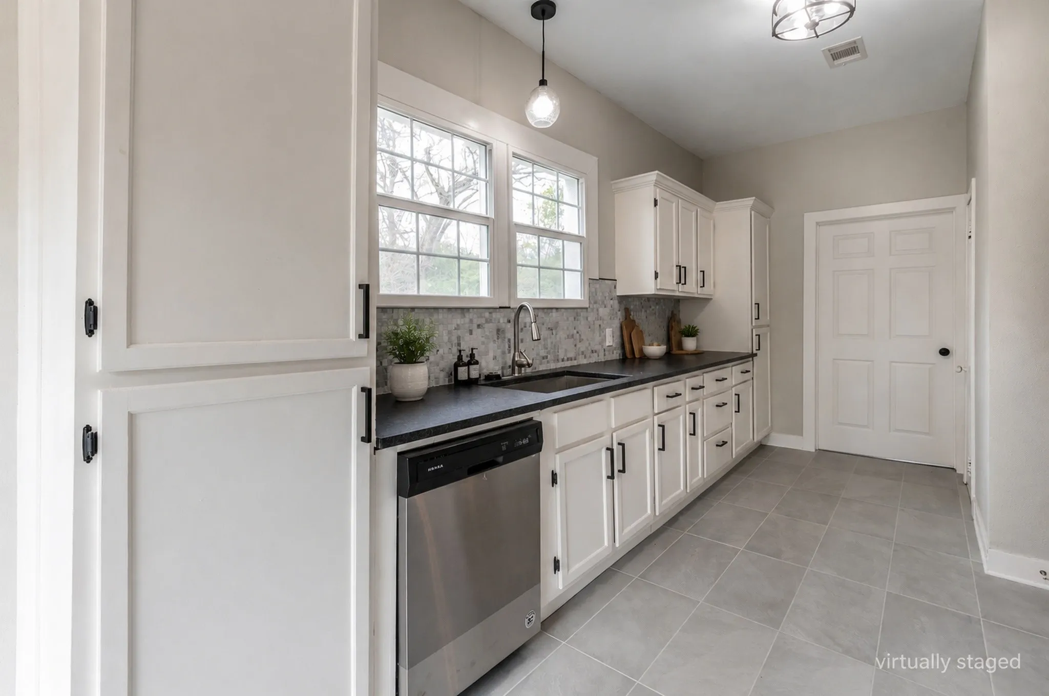Contemporary kitchen featuring white cabinetry with matte black hardware, dark countertops, and a full-height mosaic tile backsplash