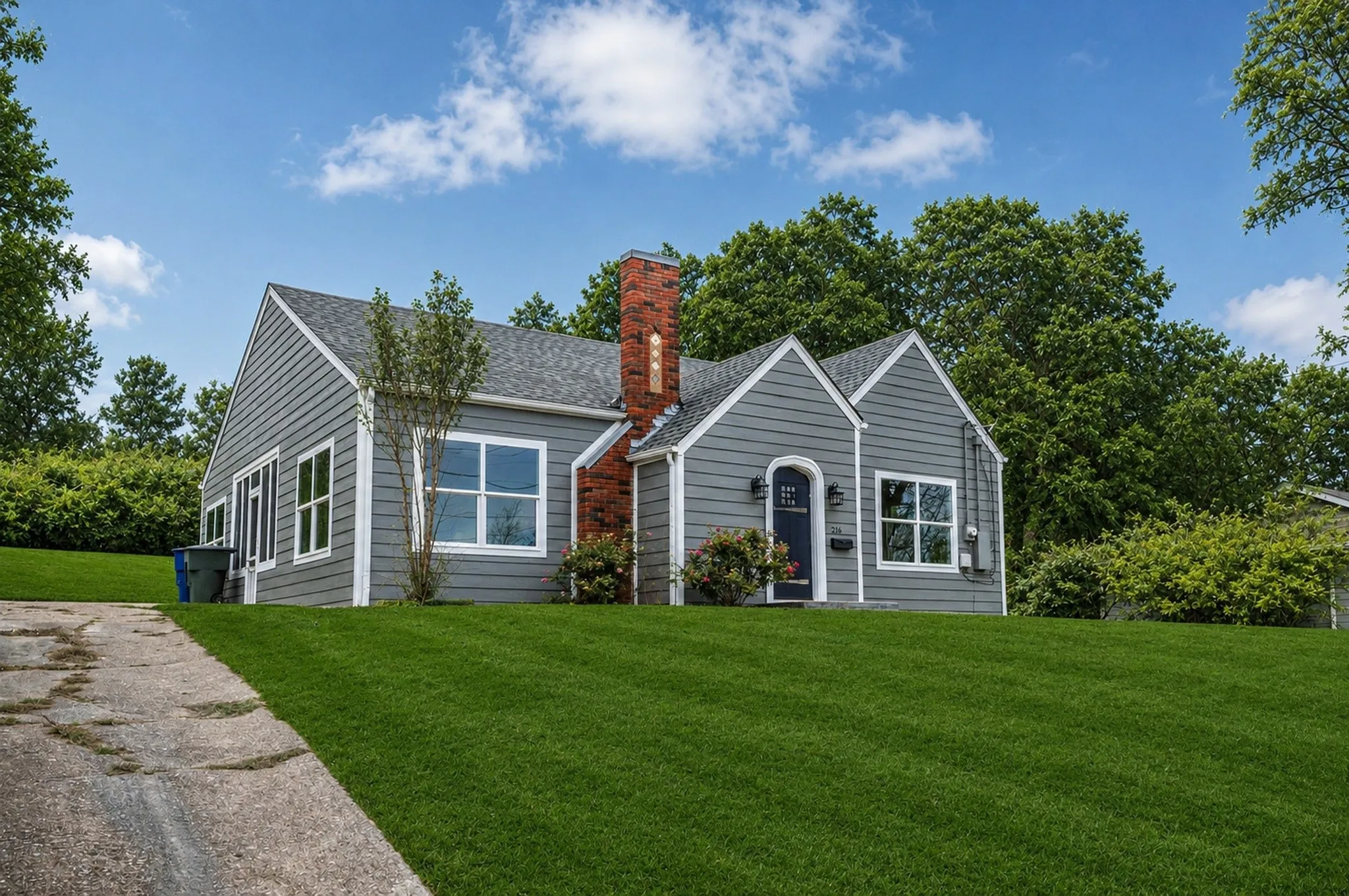 Charming single-story residence with grey siding and a dark blue arched entry door