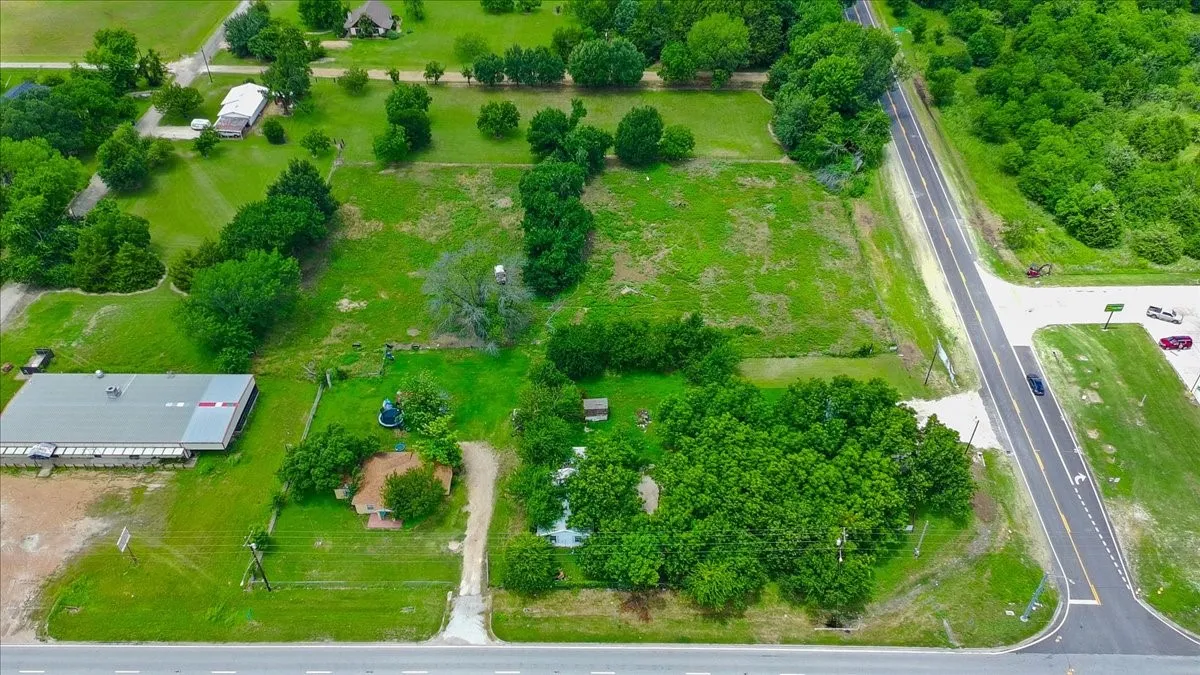 Expansive lot featuring a large commercial-style building with a metal roof, a residential structure with a brown shingled roof, a paved road frontage, and abundant mature trees