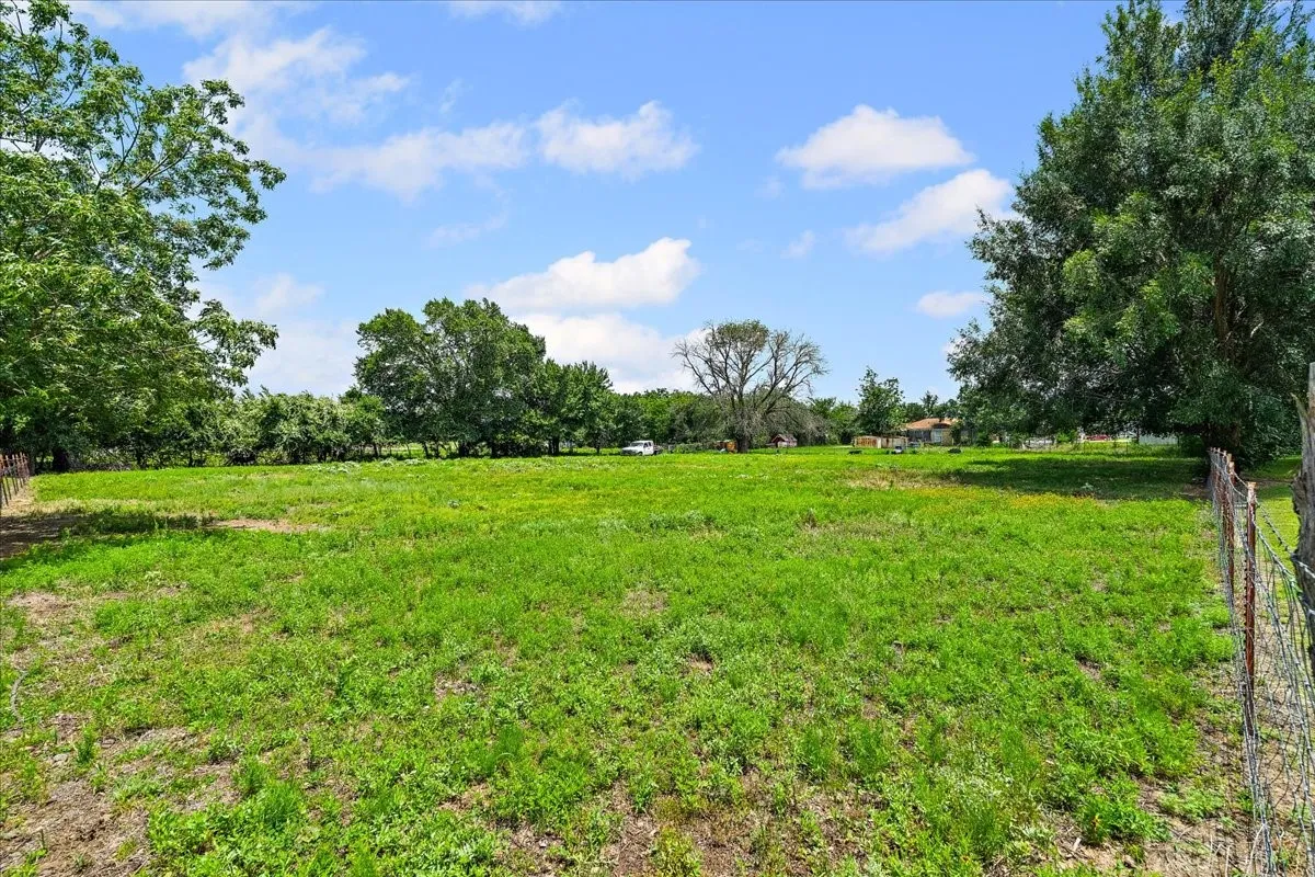 Expansive grassy lot featuring mature trees and a partial wire fence