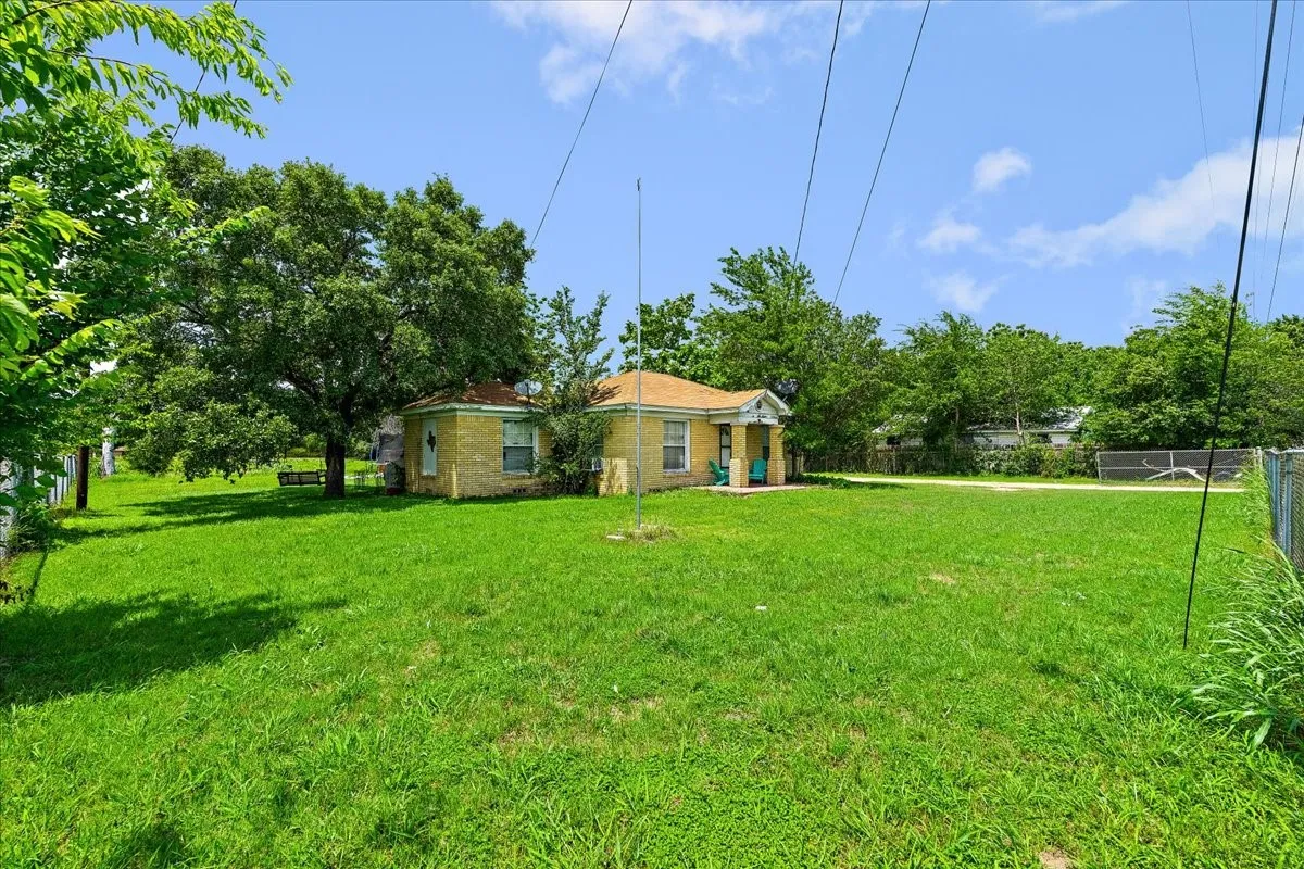 Expansive green lawn with mature trees and a two-structure property featuring light-colored brick exteriors and covered front porches