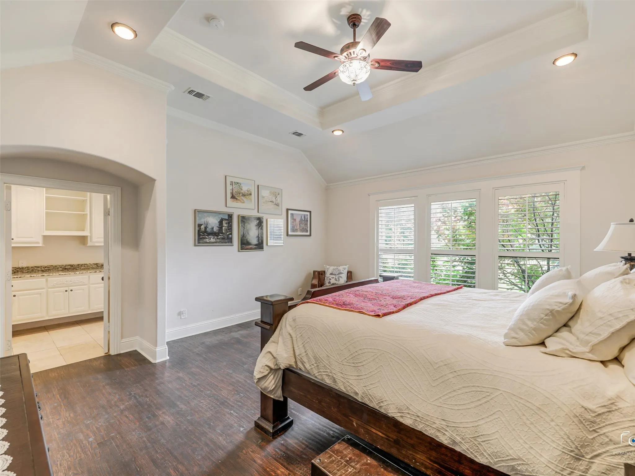 Spacious room featuring wood-finish flooring, a vaulted ceiling with decorative beams, and a ceiling fan with integrated lighting